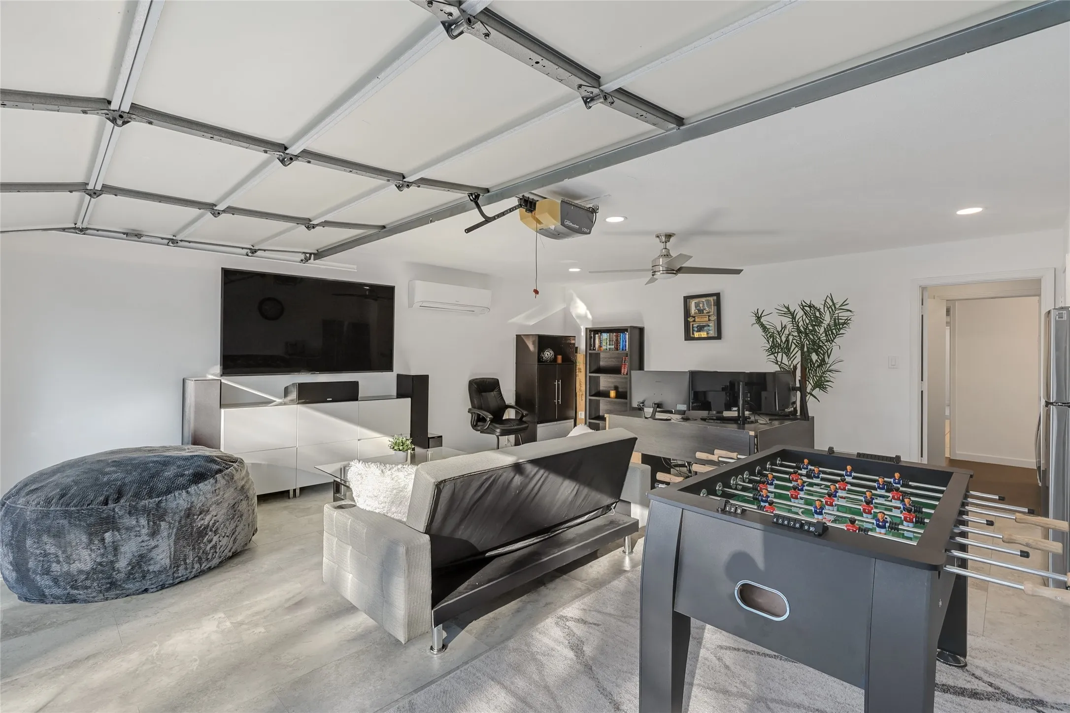 Recessed lighting, ceiling fan, white walls, and wood-finish flooring create a versatile space