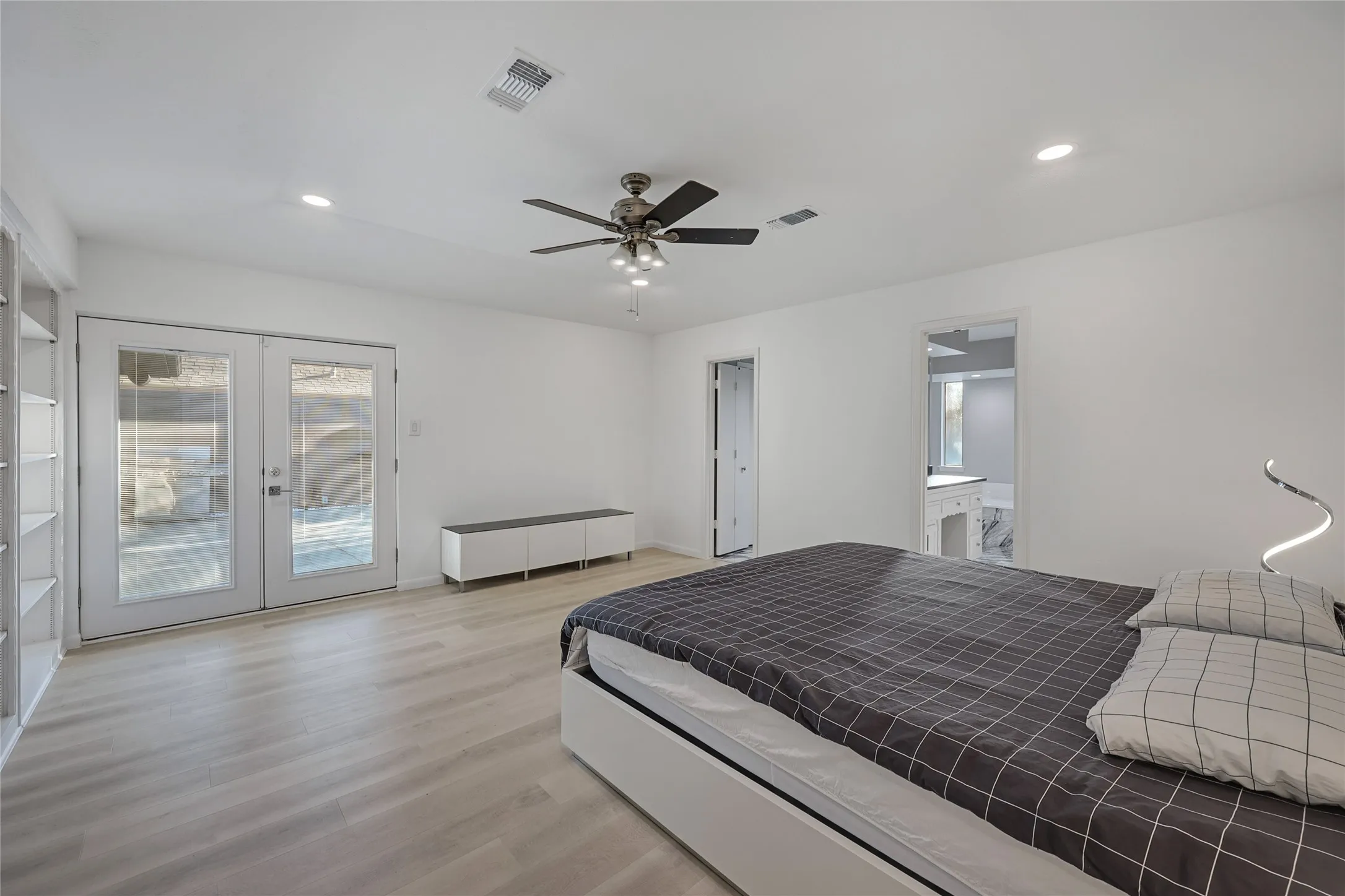 Spacious primary bedroom featuring wood-finish flooring, ceiling fan with integrated lighting, glass sliding doors opening to outdoor space, and an ensuite bathroom accessible via interior doorway
