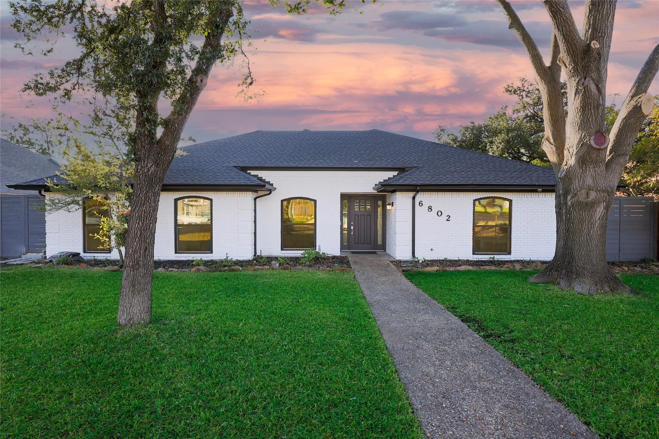 White brick exterior with dark trim, dark shingle roof, and a dark front entry door