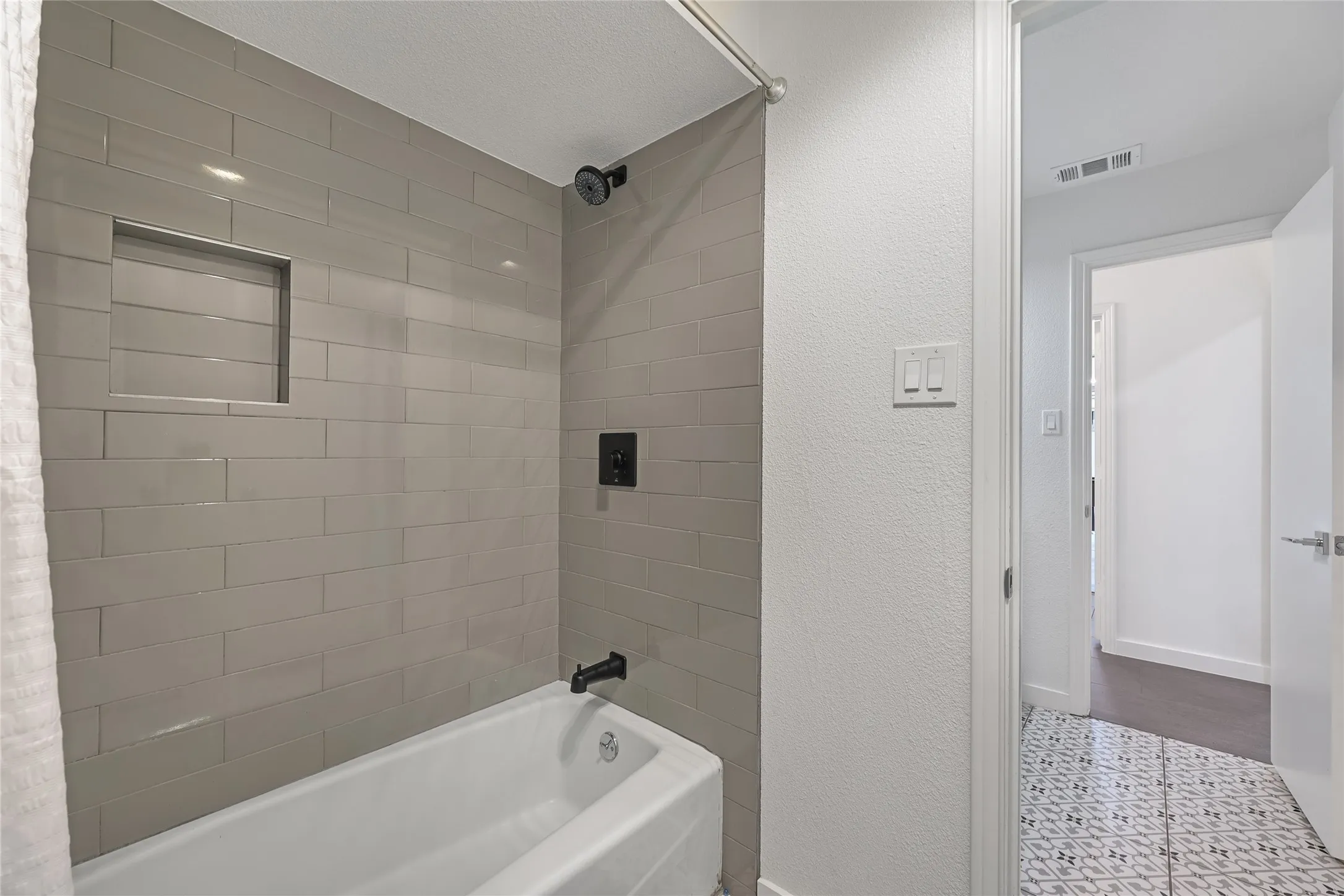 Bathtub with subway tile surround, recessed shower niche, and matte black fixtures
