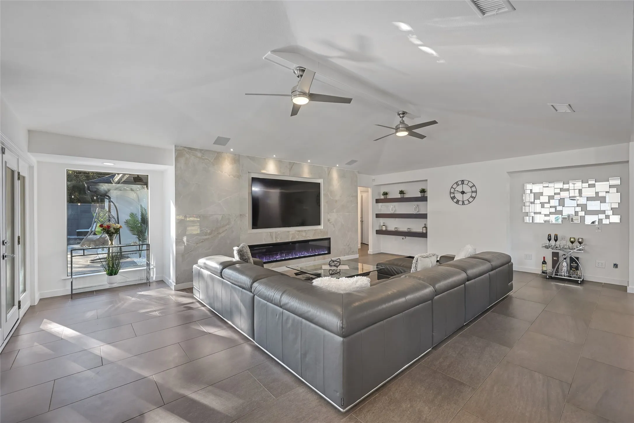 Spacious living area featuring a vaulted ceiling with dual ceiling fans, a built-in electric fireplace, and a large picture window
