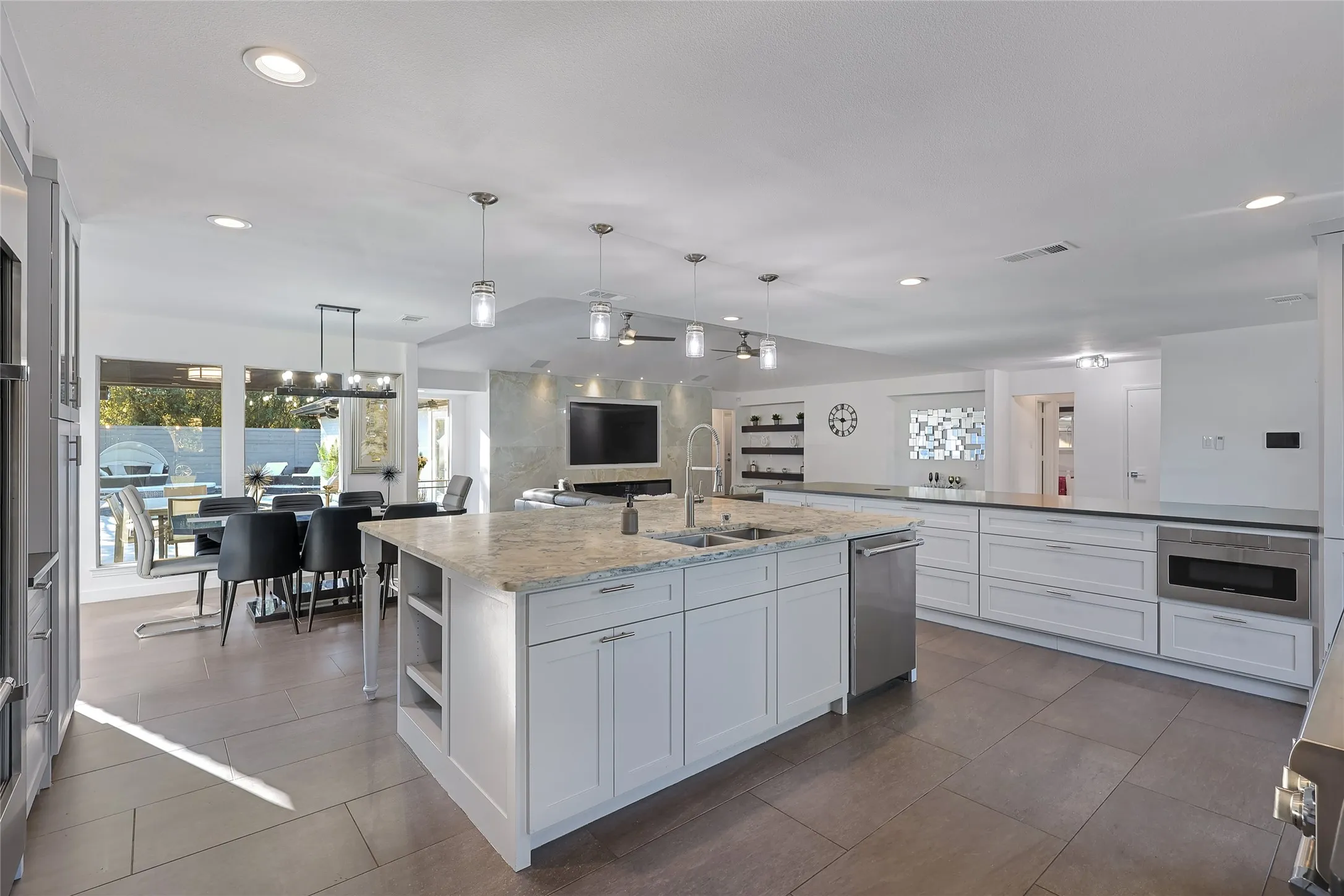 Expansive open-concept kitchen featuring a large central island with a double basin sink, white cabinetry, and recessed lighting