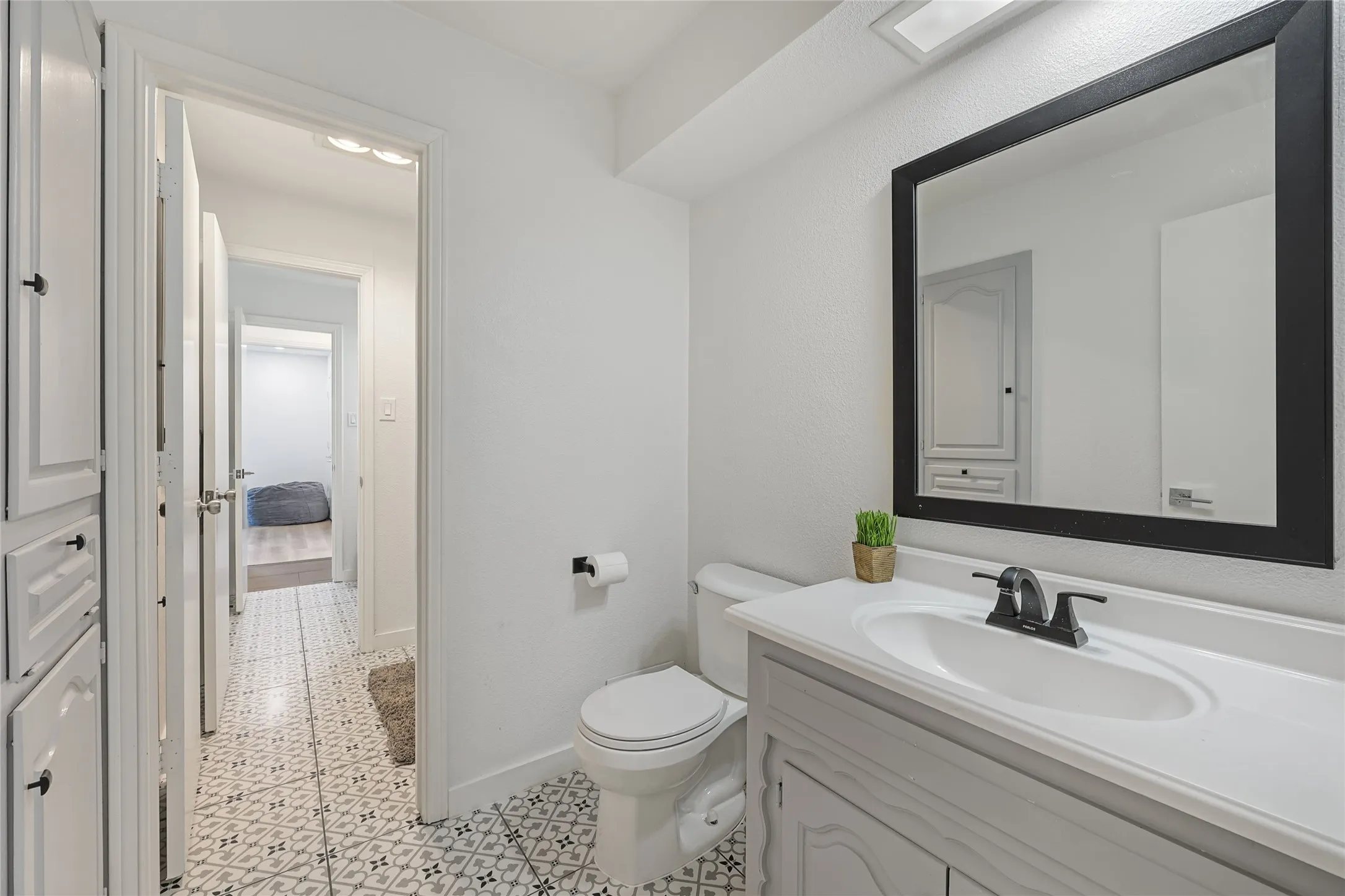 White vanity with an integrated sink and matte black faucet, framed mirror, built-in storage cabinetry, and patterned floor tile