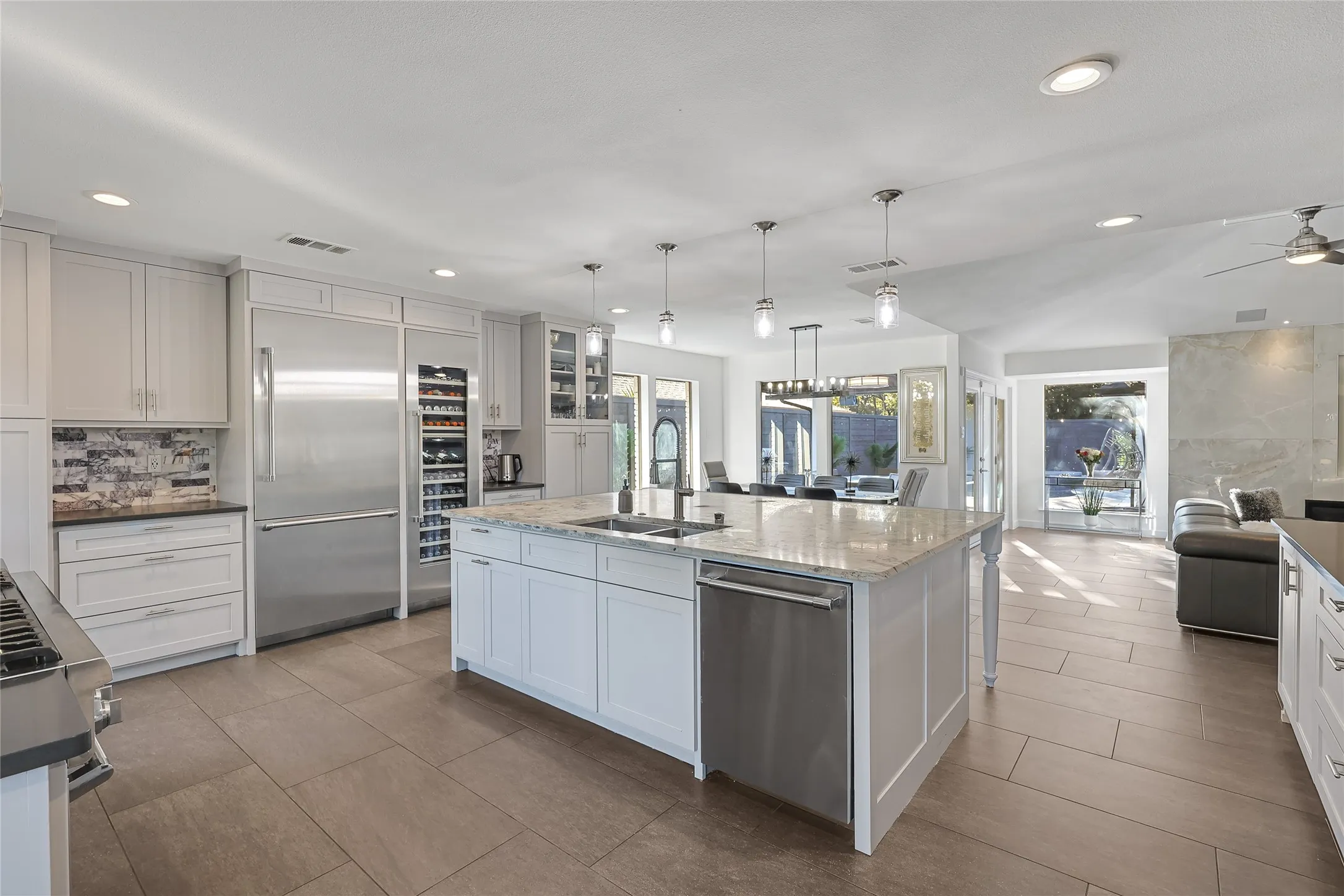 White cabinetry, stainless steel appliances, a large center island with a sink, recessed lighting, and tile flooring