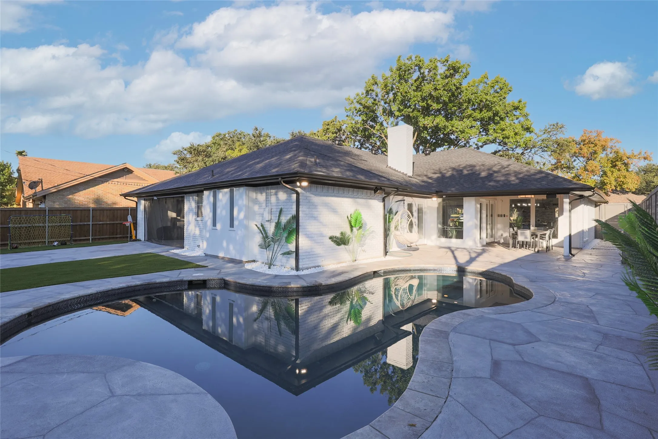Resort-style backyard featuring a dark bottom swimming pool, stone patio, artificial turf area, and a white brick exterior