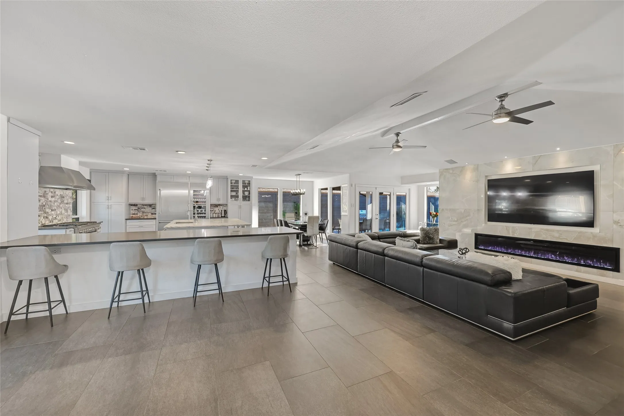 Open-concept living area with large-format tile flooring, a built-in linear fireplace, and a spacious kitchen island with seating