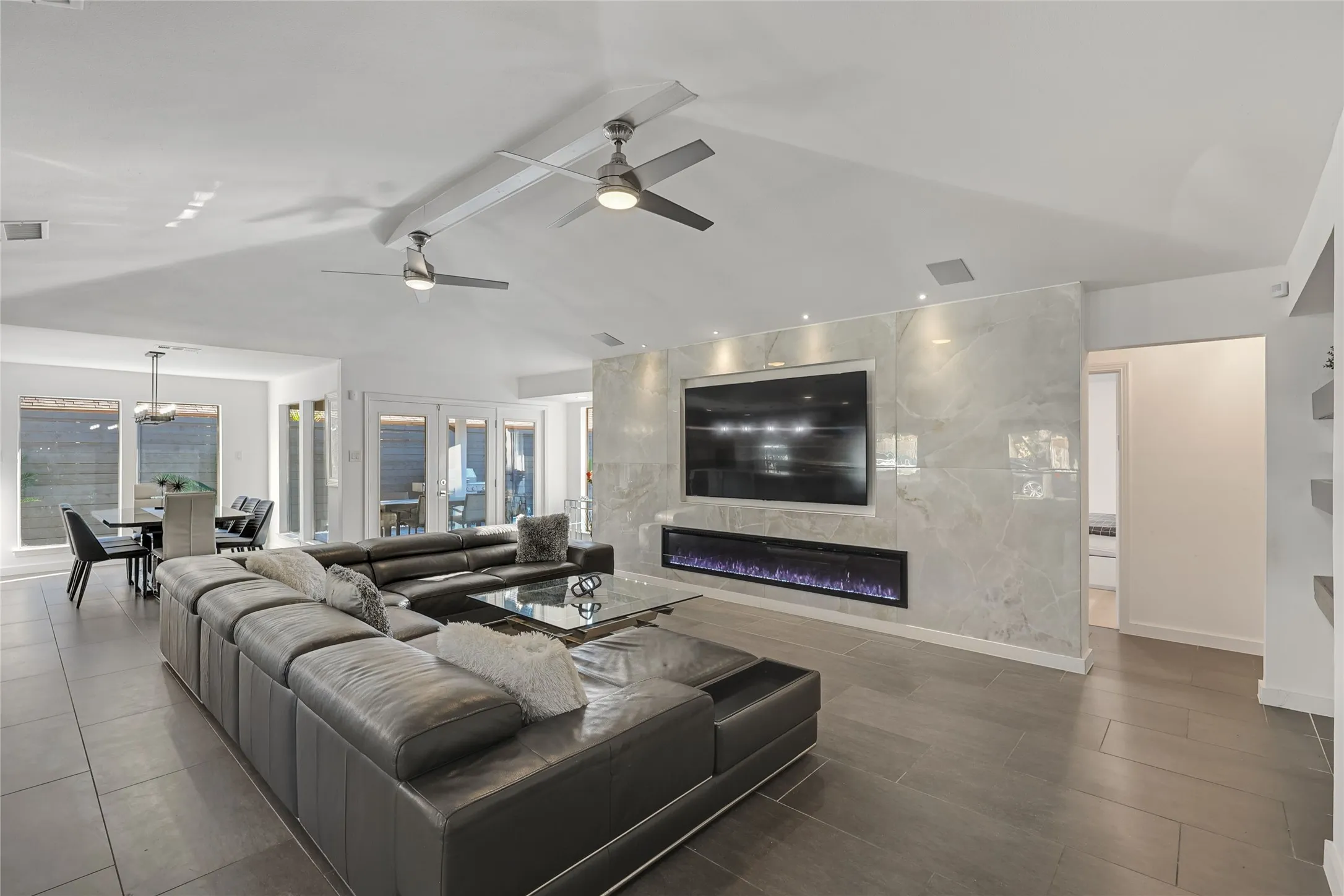 Vaulted ceilings with recessed lighting, tile flooring, and a linear electric fireplace integrated into a floor-to-ceiling tile accent wall