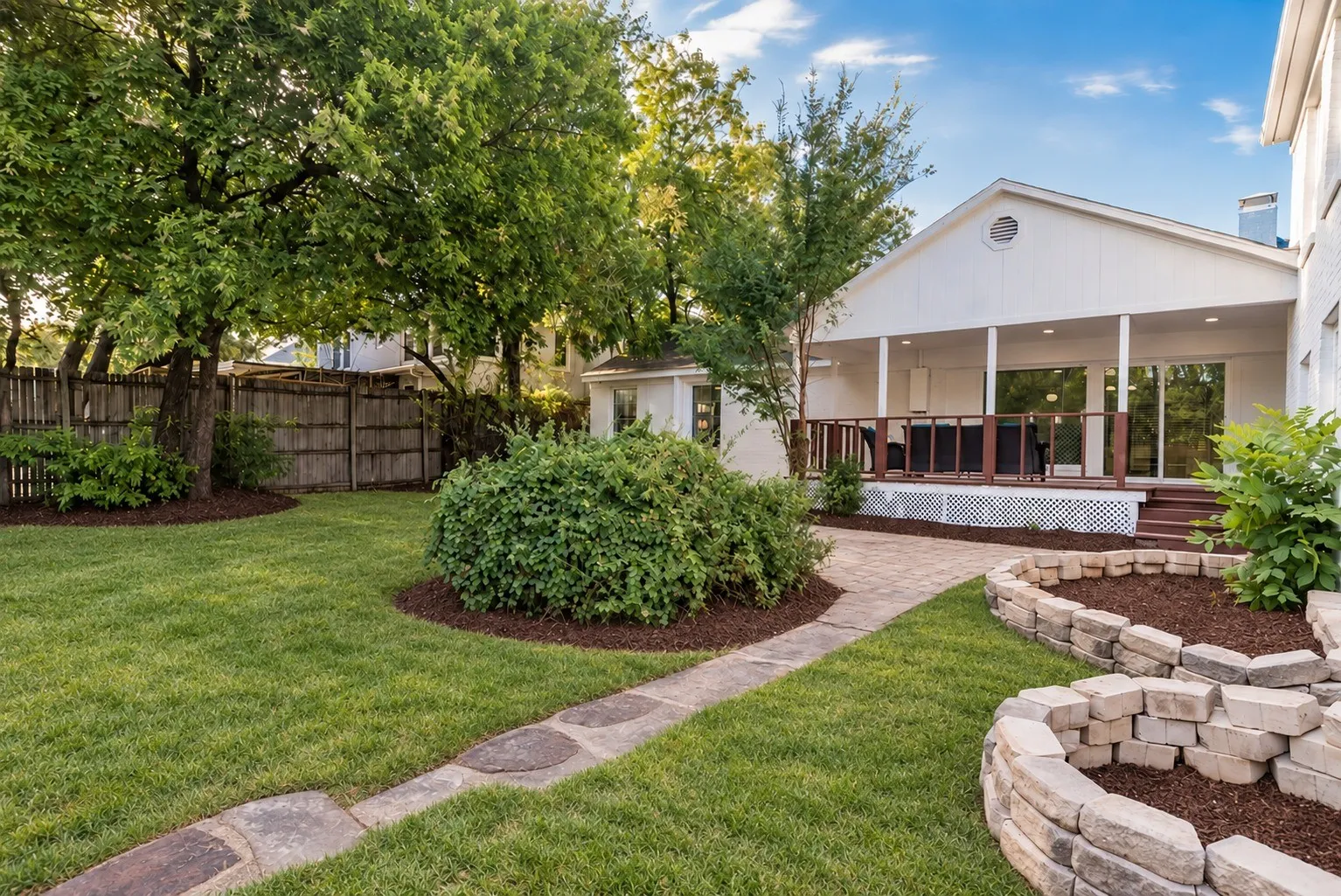 Backyard with green lawn, mulched beds, stone planter and stone walkway