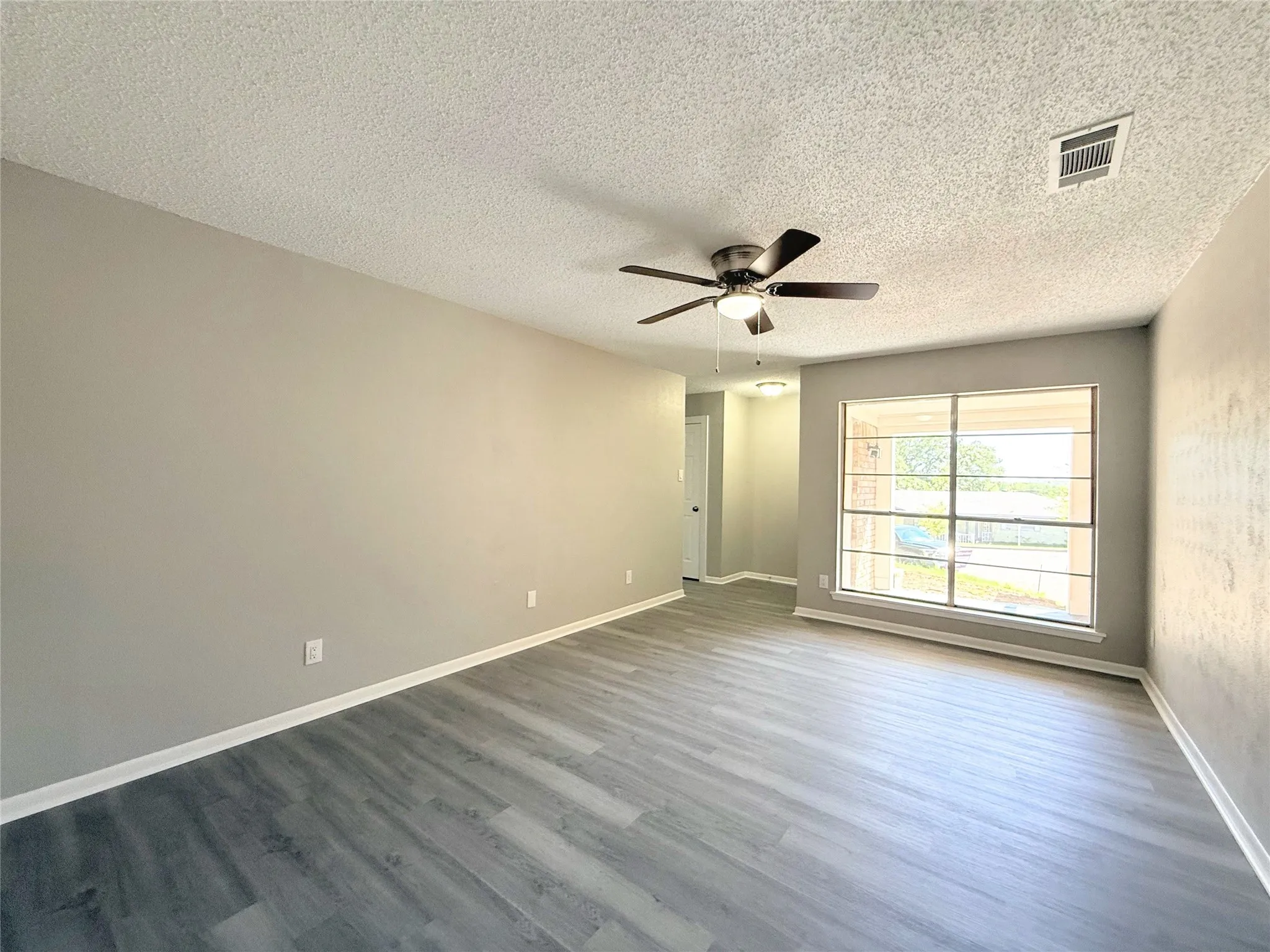 Wood-finish flooring, neutral wall paint, and a ceiling fan with integrated lighting