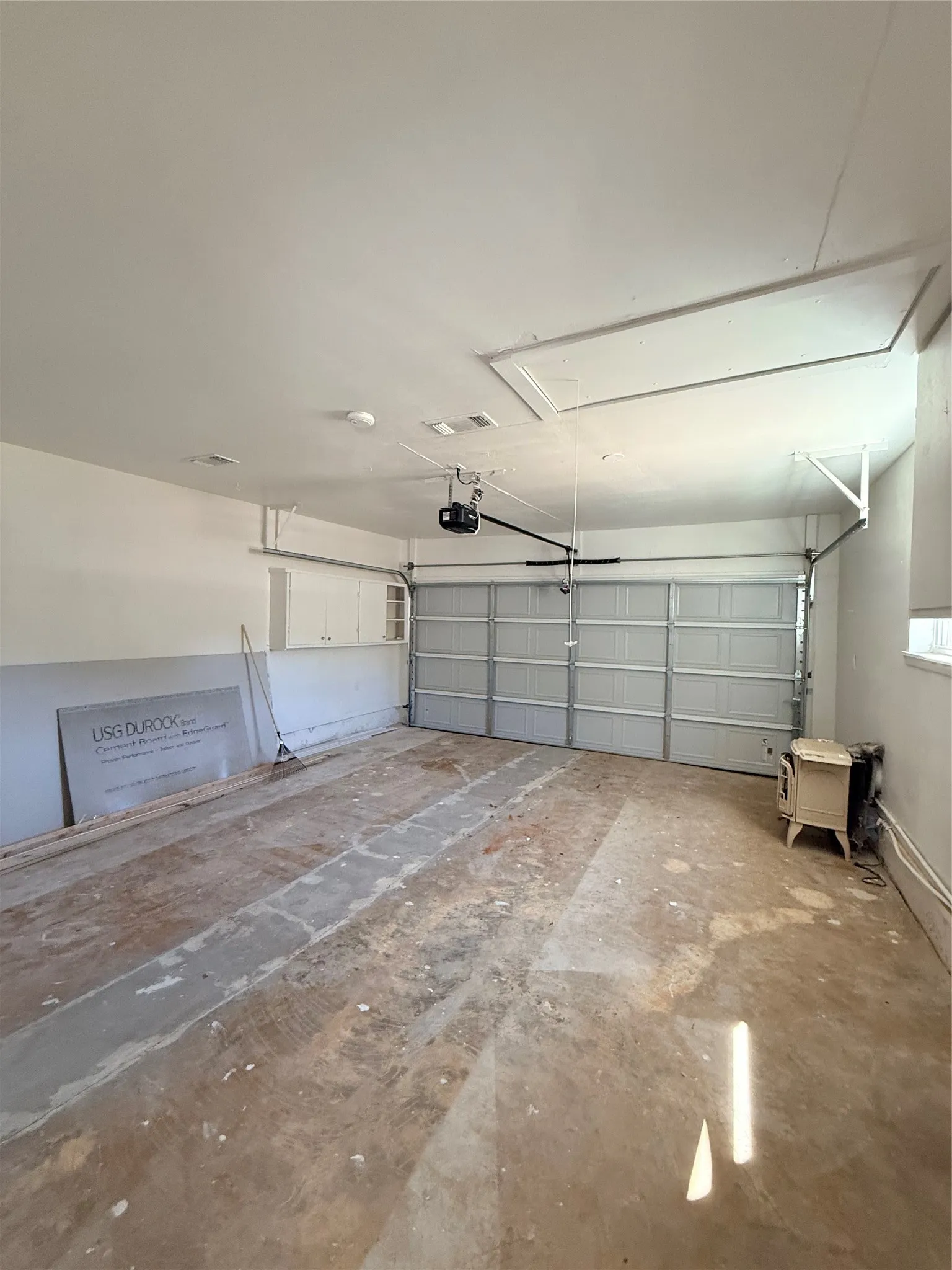 Garage with an automatic overhead door, overhead lighting, and built-in white cabinetry