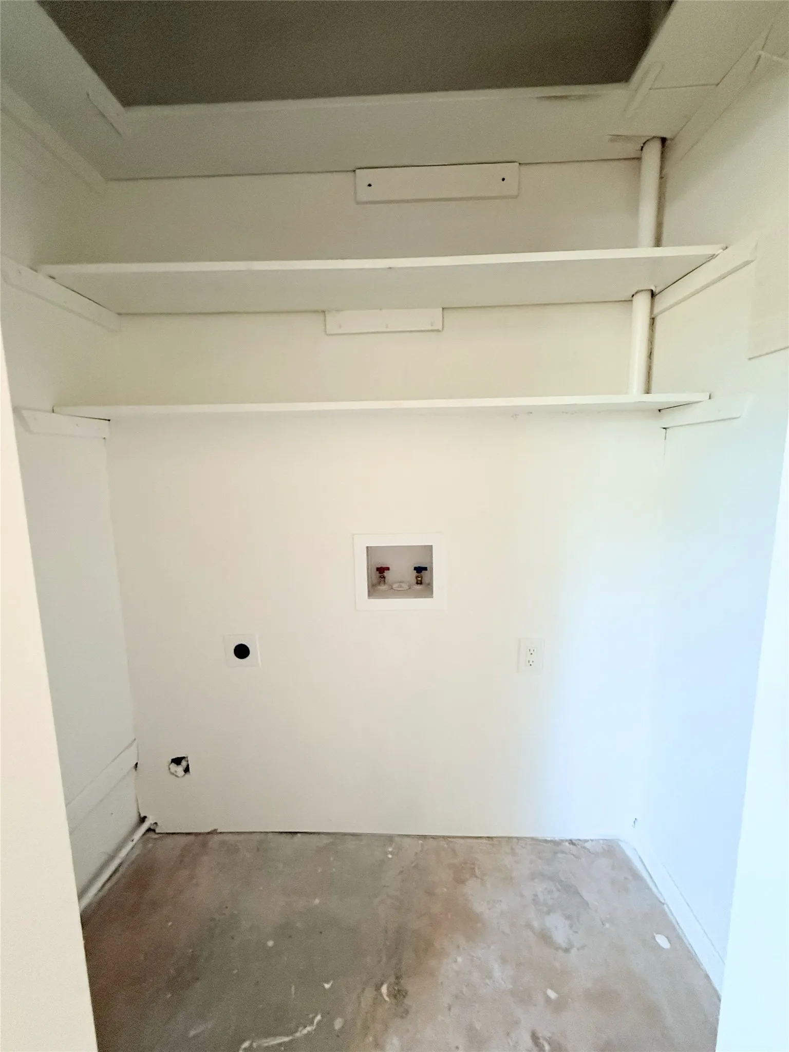 Utility closet with built-in shelving, laundry hookups, and a concrete floor