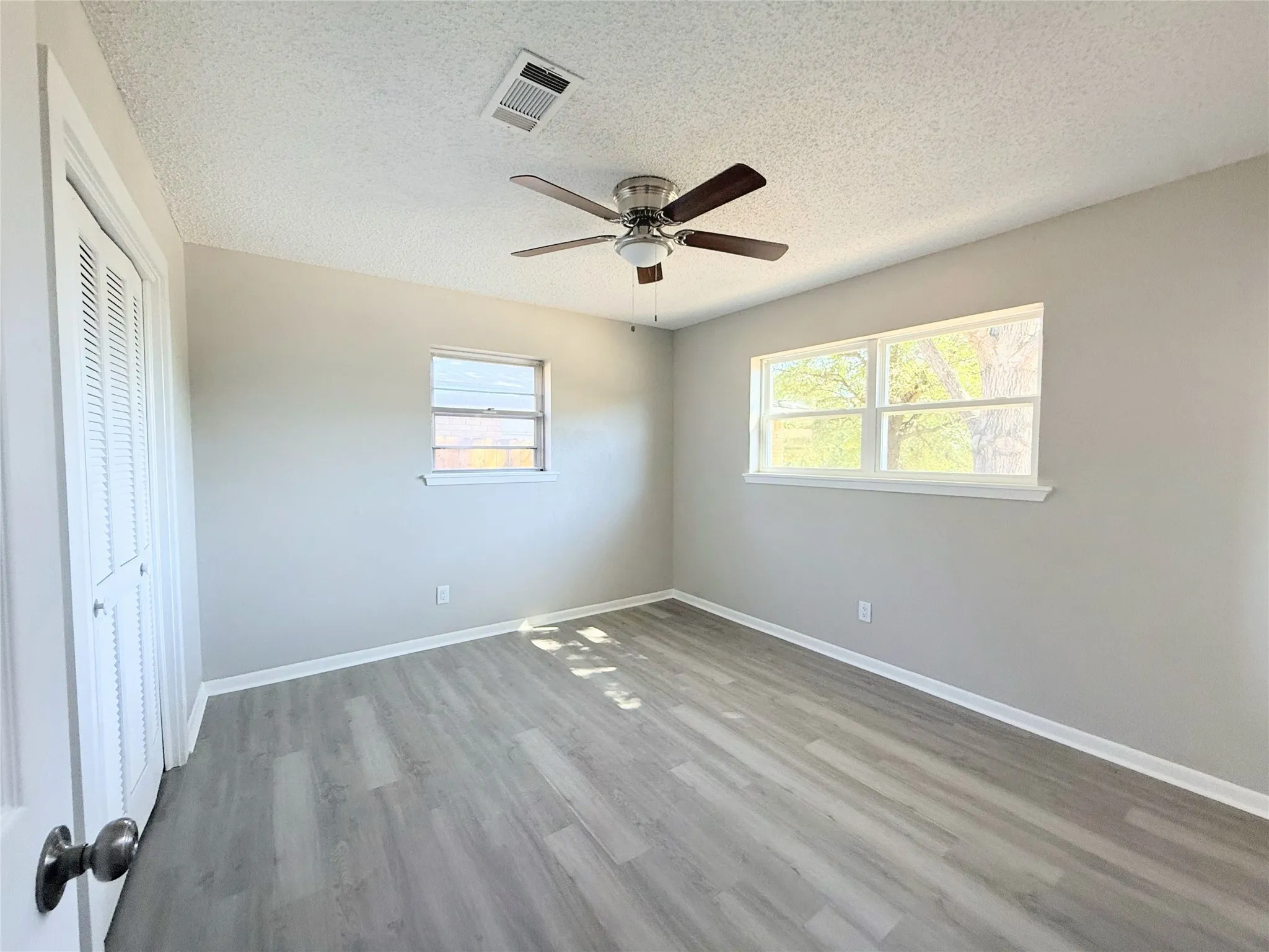 Wood-finish flooring, neutral wall tones, two windows with white trim, a louvered closet door, and a ceiling fan