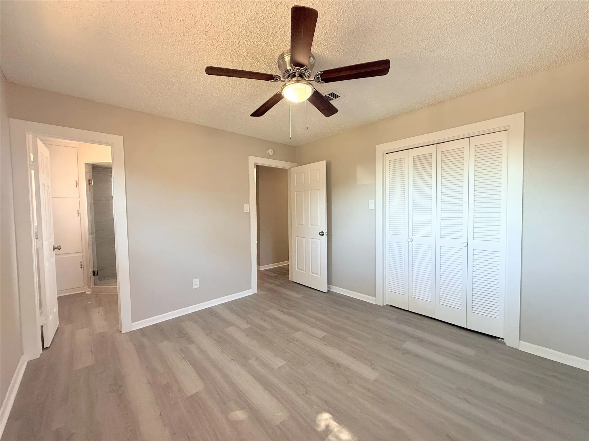 Spacious room featuring wood-finish flooring, a ceiling fan, and bi-fold closet doors
