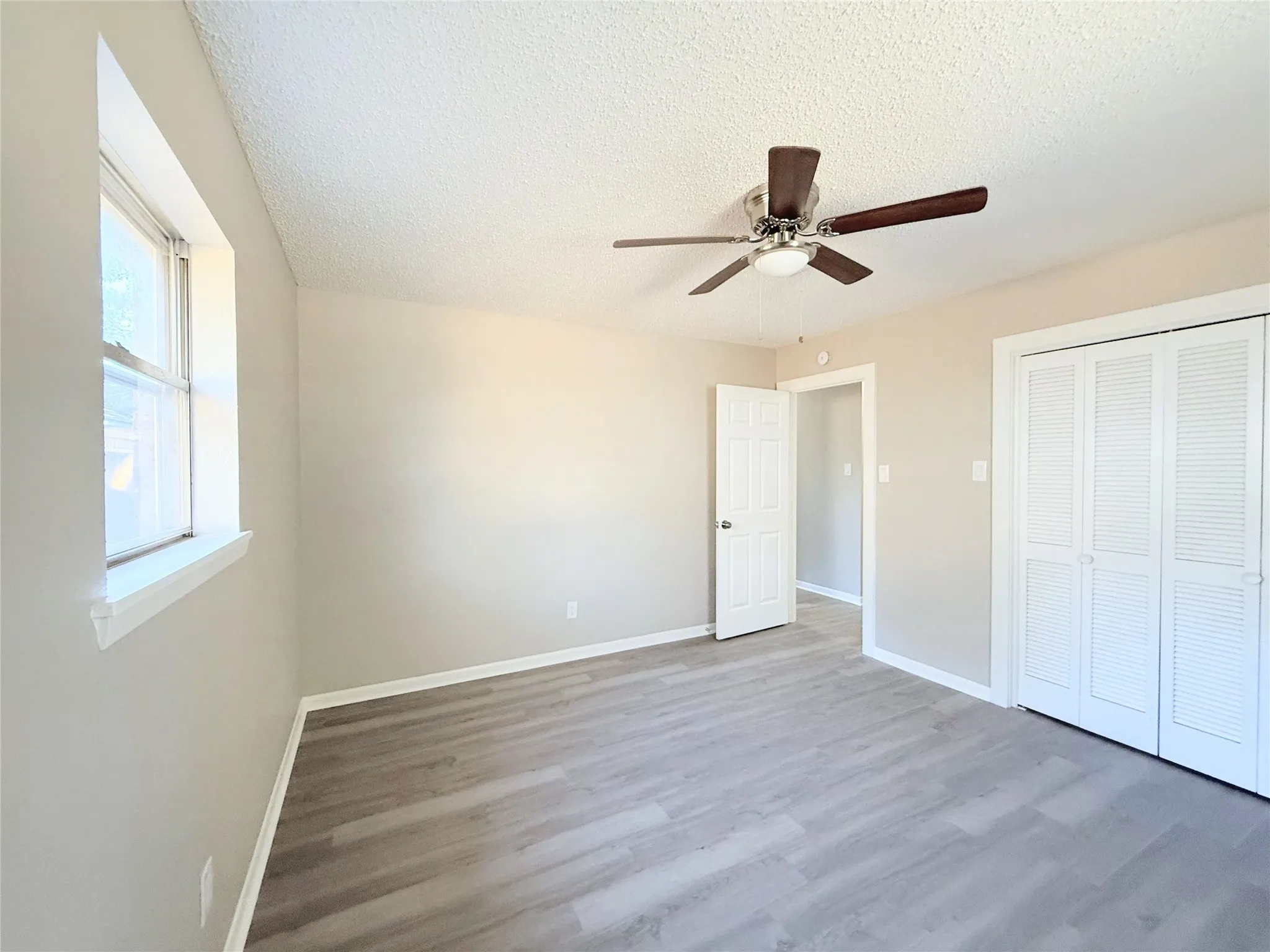 Wood-finish flooring, neutral wall tones, ceiling fan with integrated lighting, window with white trim, bi-fold closet doors