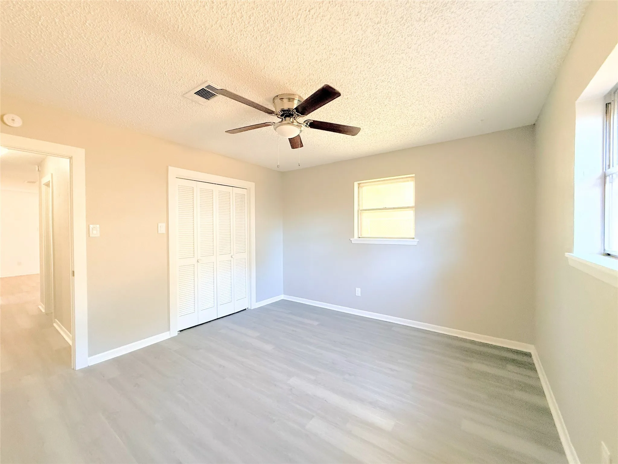 Wood-finish flooring, ceiling fan with integrated lighting, window with trim, and bi-fold closet doors
