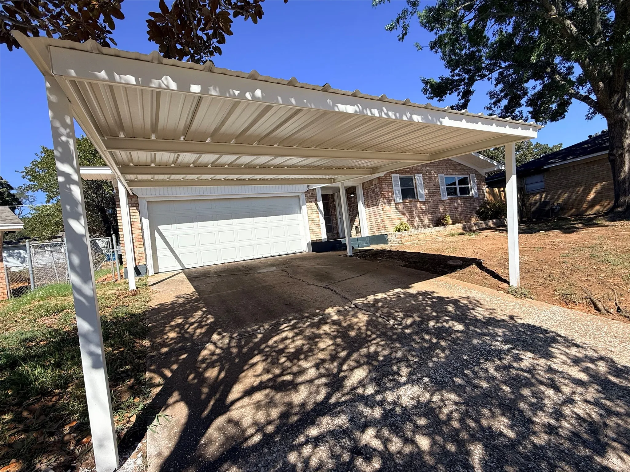 White aluminum pergola with louvered roof panels extending over the driveway, providing shade and weather protection