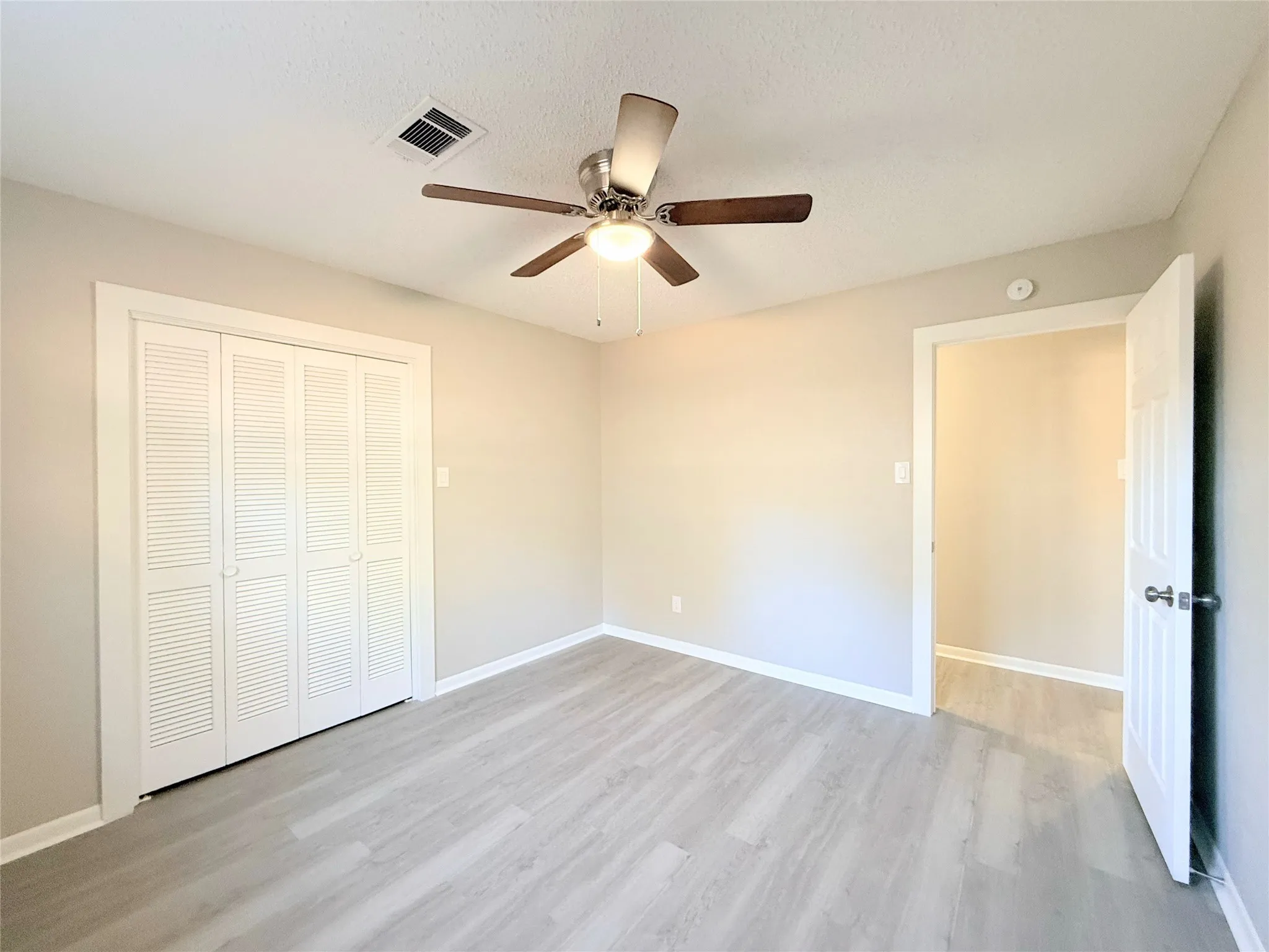 Light-toned walls, wood-finish flooring, ceiling fan, bi-fold closet doors, and white trim