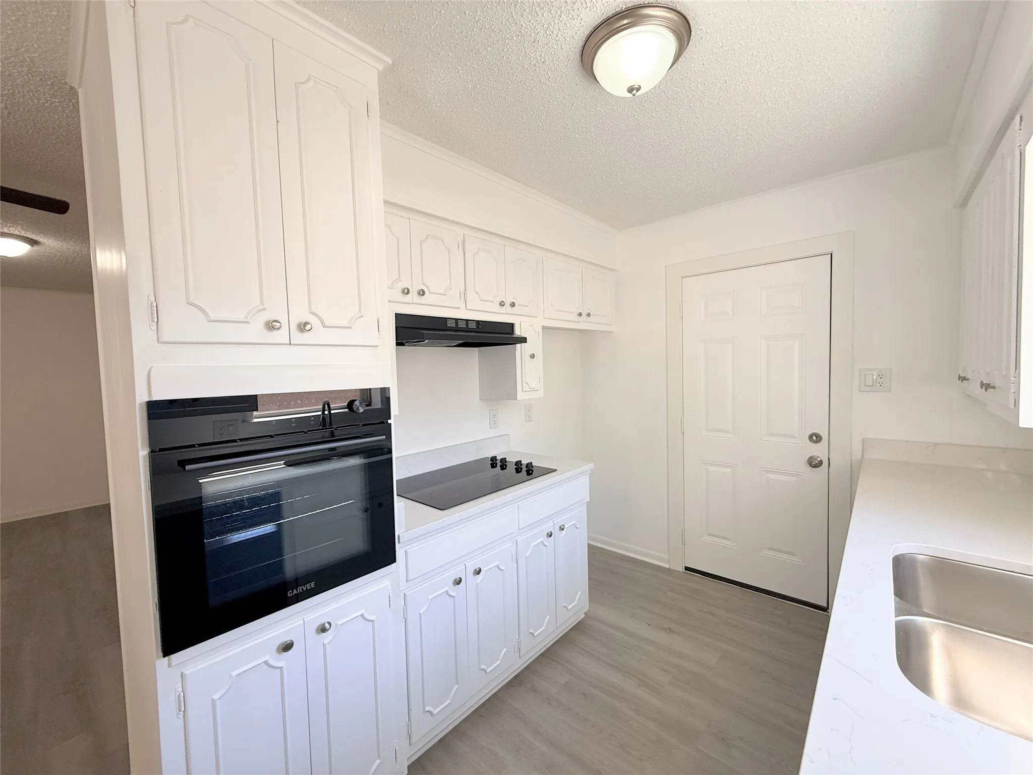 White cabinetry, integrated oven, cooktop, stainless steel sink, and wood-finish flooring