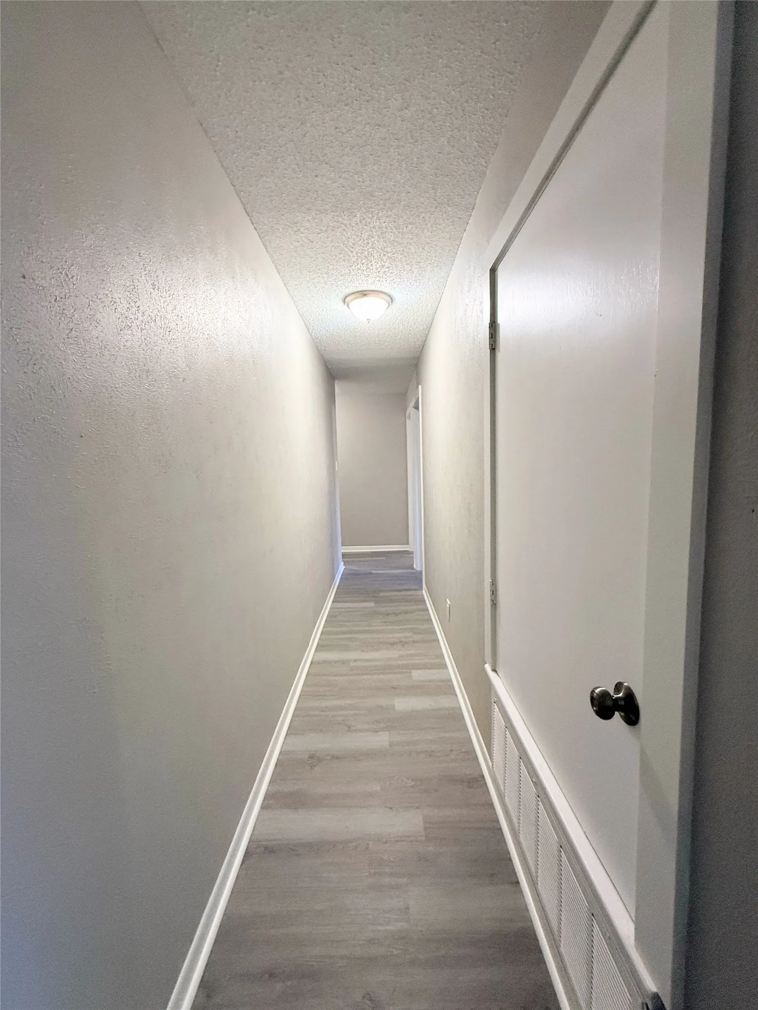 Hallway featuring wood-finish flooring, textured ceiling, recessed lighting, and clean white walls with wainscoting detail