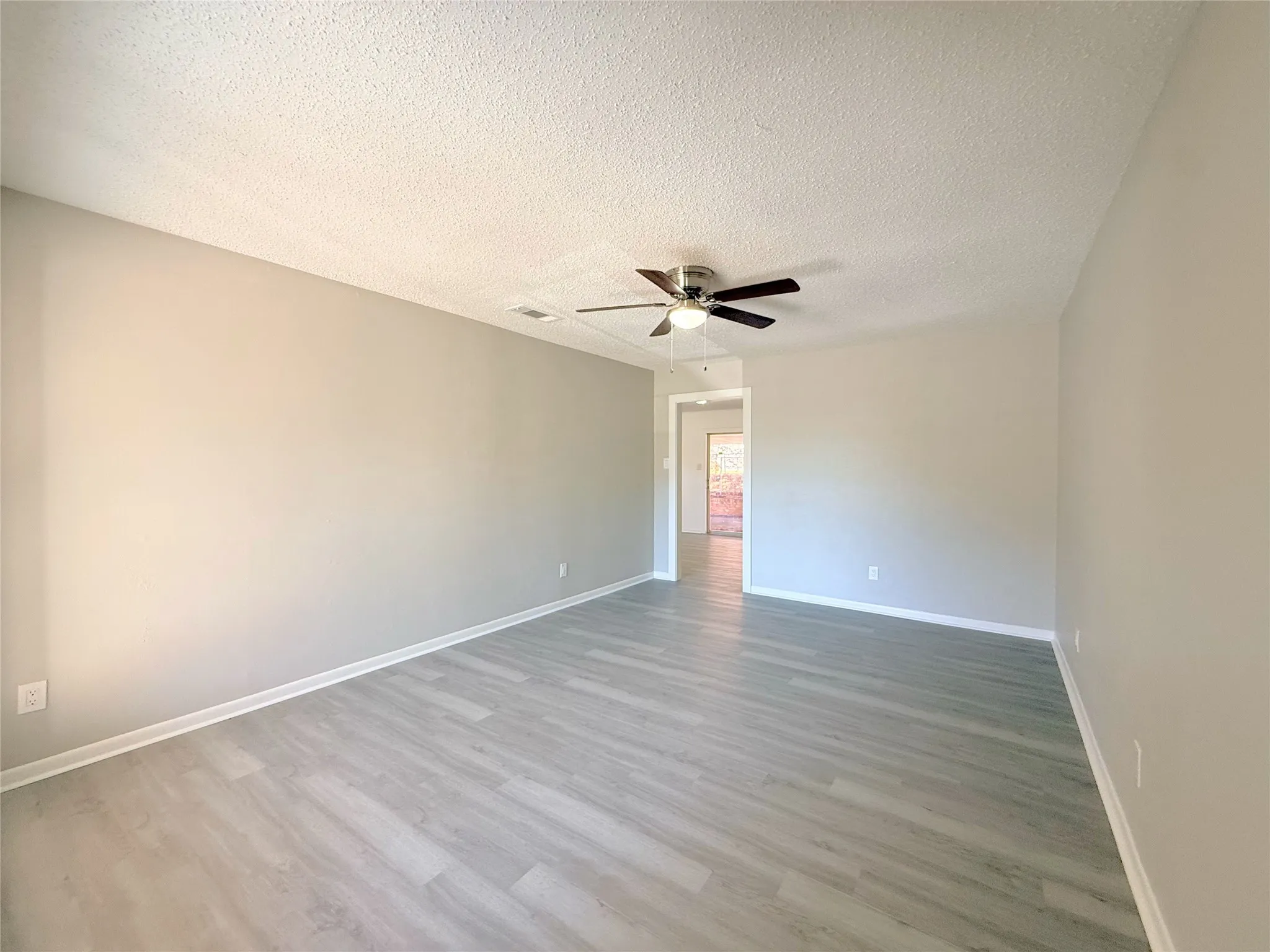 Spacious room featuring light wood-finish flooring, neutral wall paint, and a ceiling fan with integrated lighting