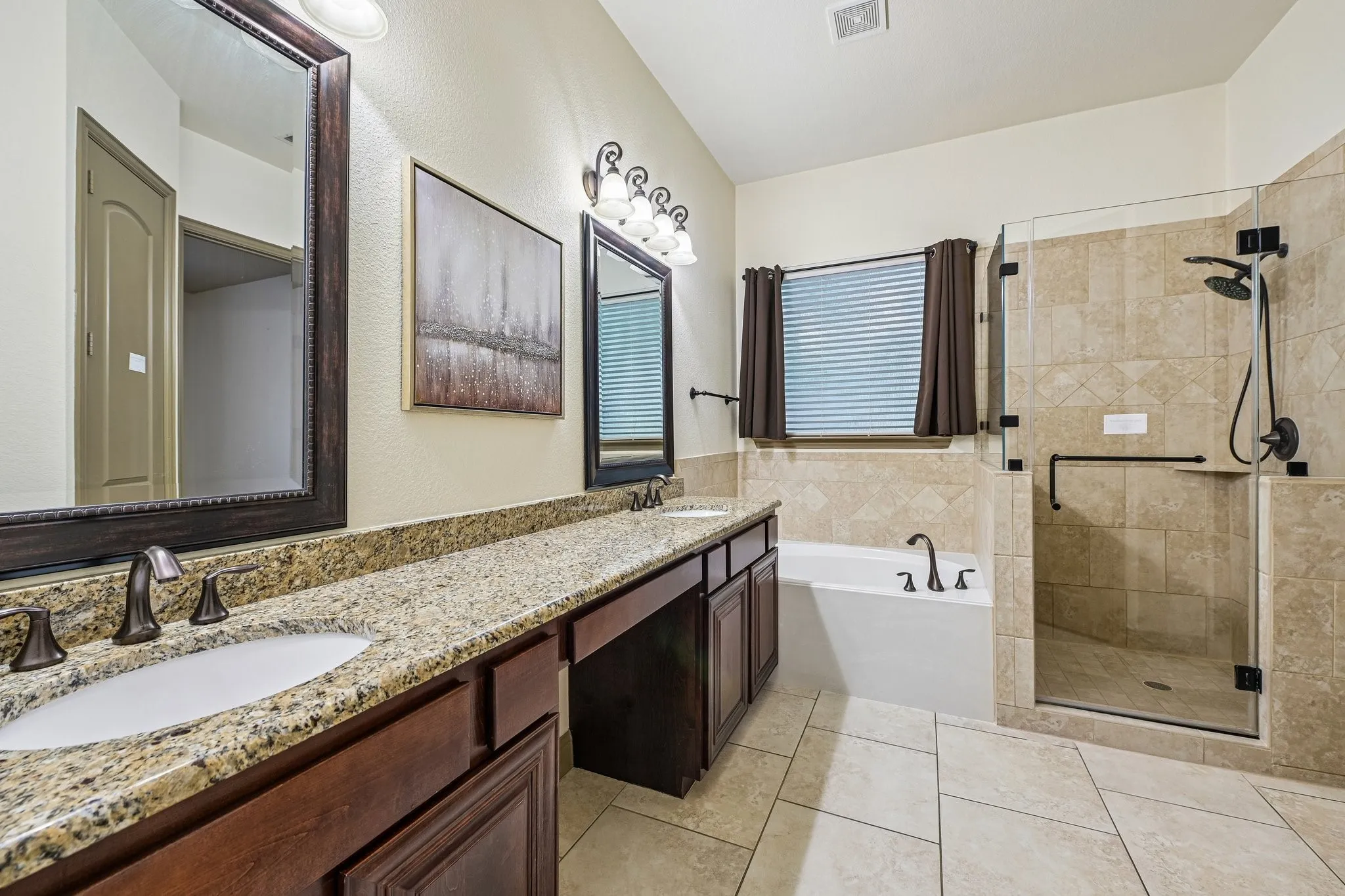 Granite countertop with undermount sink, oil-rubbed bronze faucet, dark wood vanity cabinetry, full-height tile shower surround, and built-in shower shelf