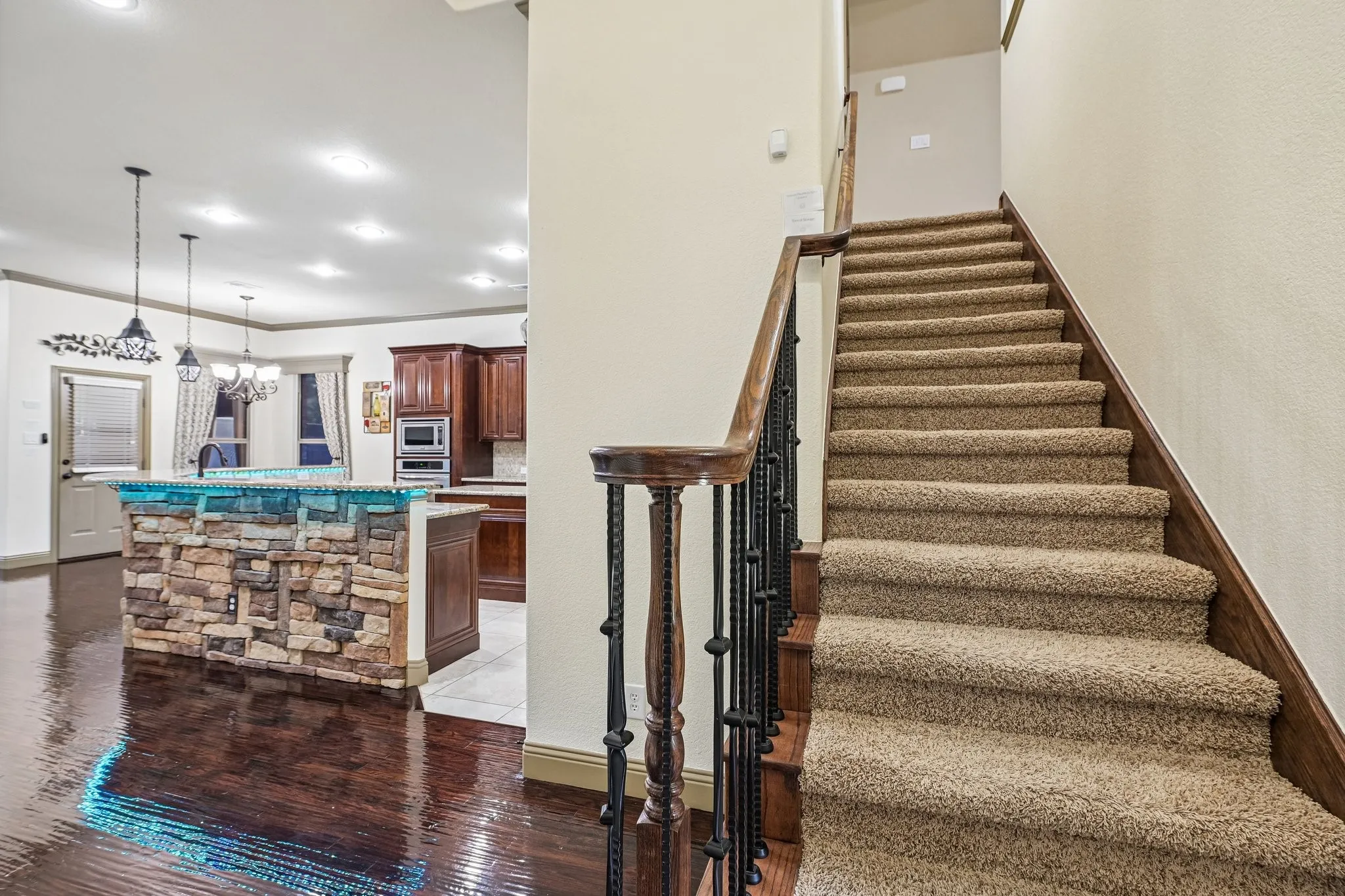 Wood-finish flooring, stone-clad kitchen island, recessed lighting, stained wood cabinetry, and carpeted staircase with wrought iron balusters