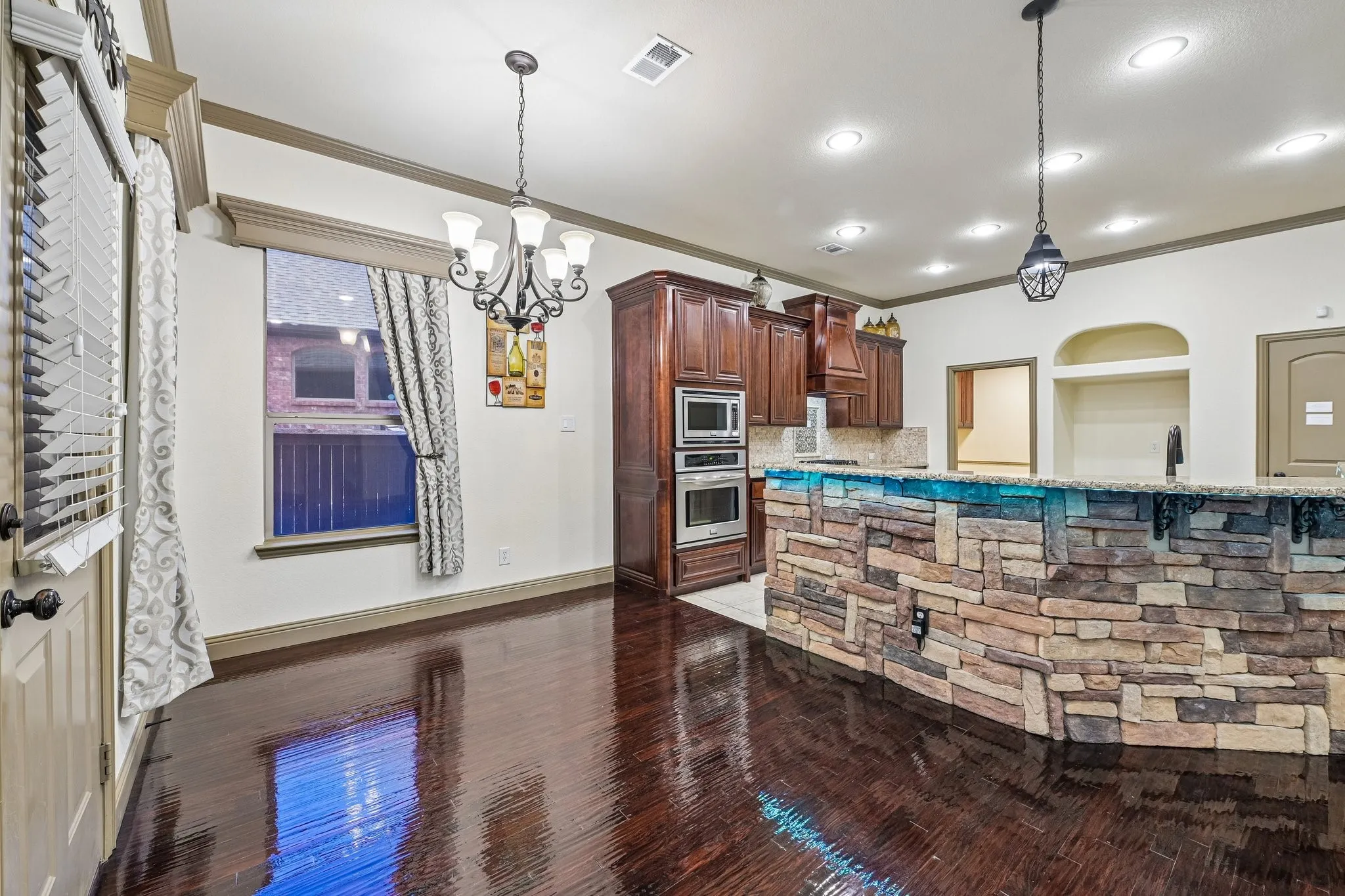 Rich wood-finish flooring, stone-clad kitchen island, dark wood cabinetry, stainless steel double oven, and recessed lighting