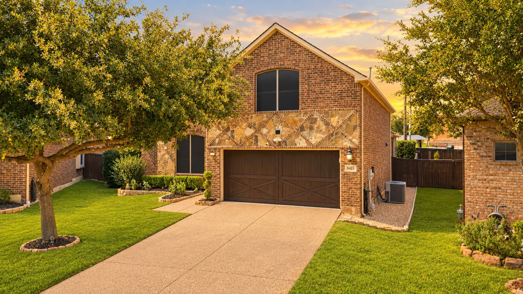 Immaculate home showcasing a wide concrete driveway, two-car garage with dark finish doors, and manicured lawn framed by mature landscaping