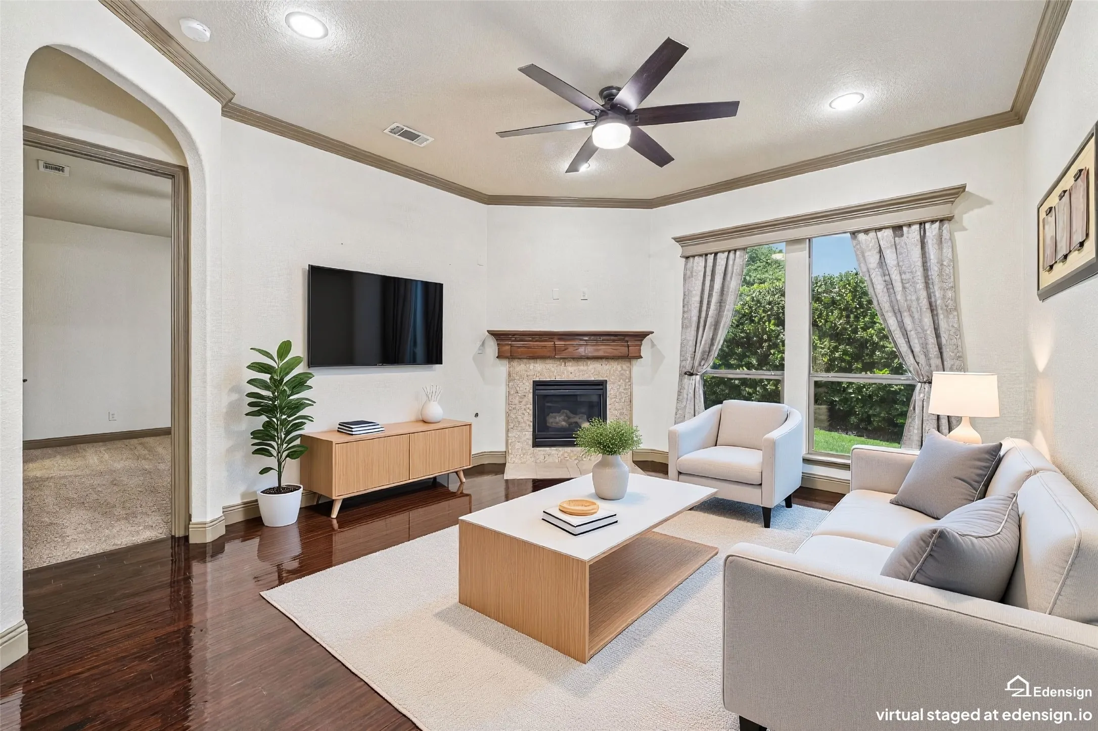 Sophisticated living room featuring a coffered ceiling with recessed lighting and ceiling fan, wood-finish flooring throughout, a gas fireplace with brick surround and mantel, and expansive windows with natural light and custom drapery. Virtually Staged.