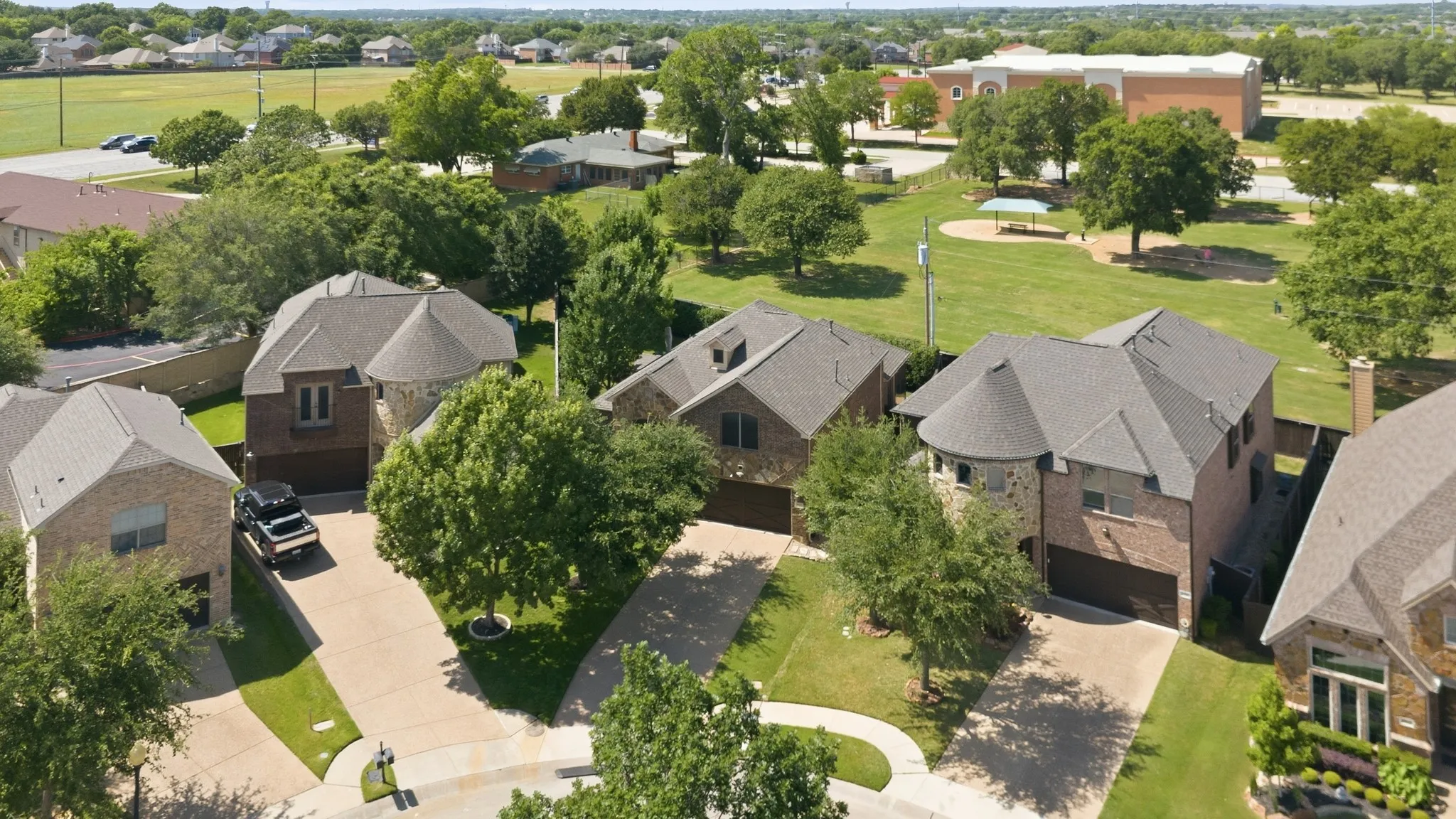 Aerial perspective showcasing residential properties with brick and stone exteriors, asphalt shingle roofs, attached garages, and mature landscaping