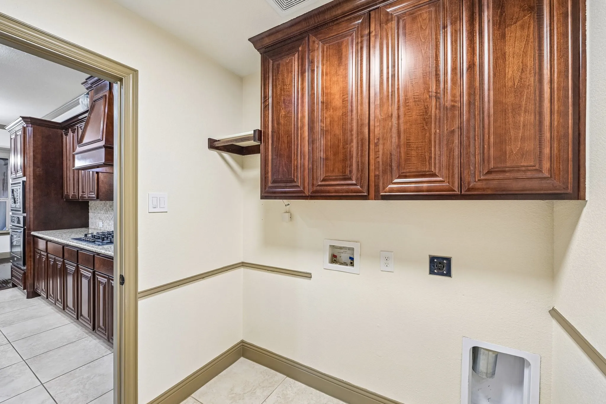 Wood-finish cabinetry with panel doors, wall-mounted shelving, and tile flooring