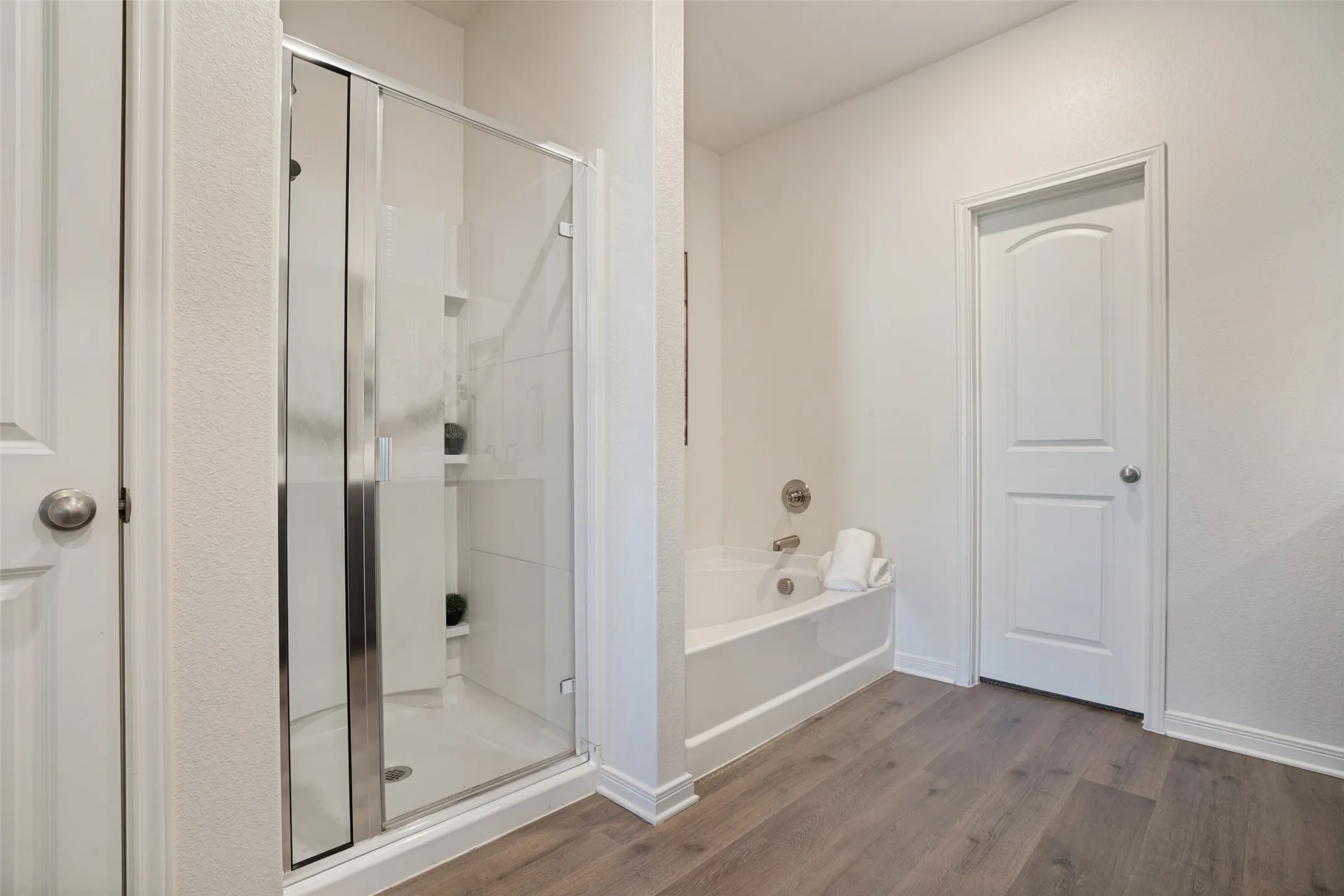Glass-enclosed shower with built-in shelving, separate soaking tub, and wood-finish flooring