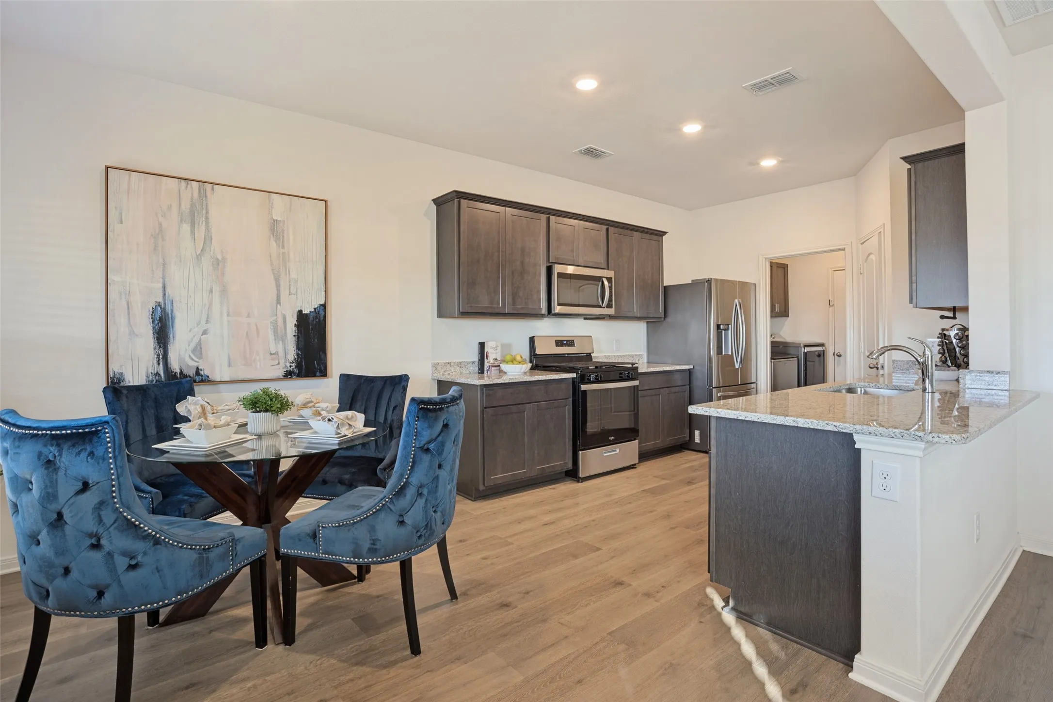 Open-concept kitchen featuring wood-finish flooring, dark wood cabinetry, stainless steel appliances, and light-toned countertops