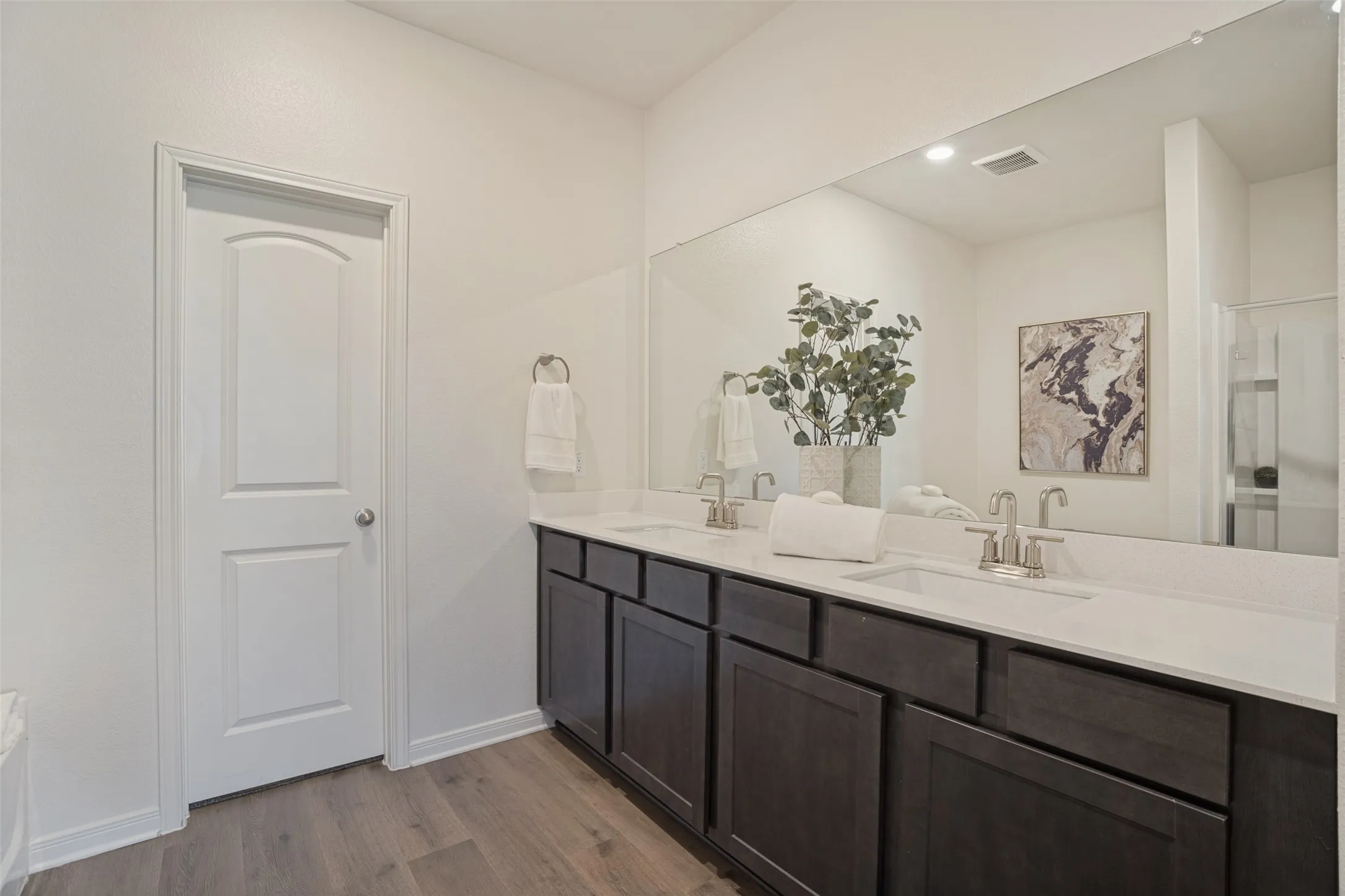 Dual vanity with integrated sinks and brushed nickel faucets, dark wood-finish cabinetry, a large wall-mounted mirror, and wood-finish flooring