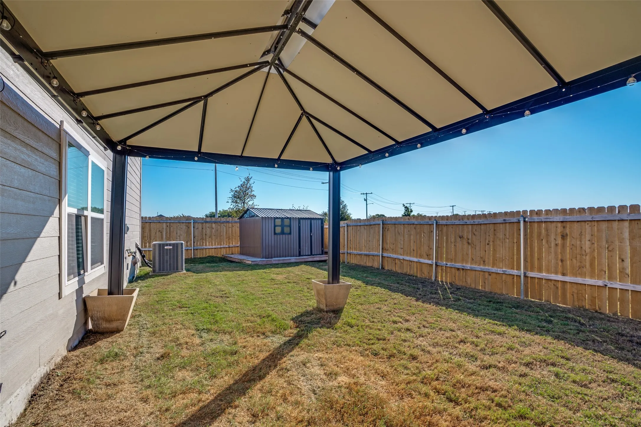 Expansive backyard featuring a covered patio, privacy fencing, and a storage shed