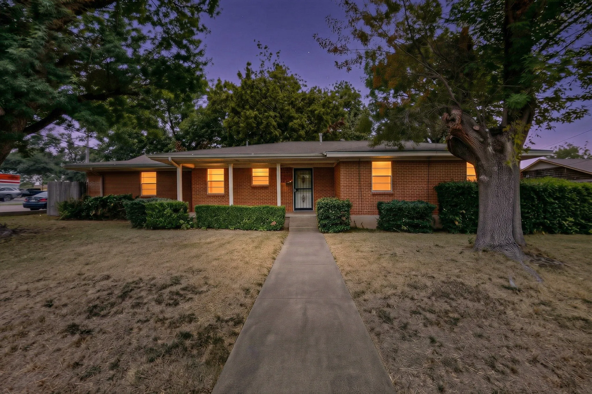 Brick exterior with a covered porch entry, mature front yard trees, and a concrete pathway