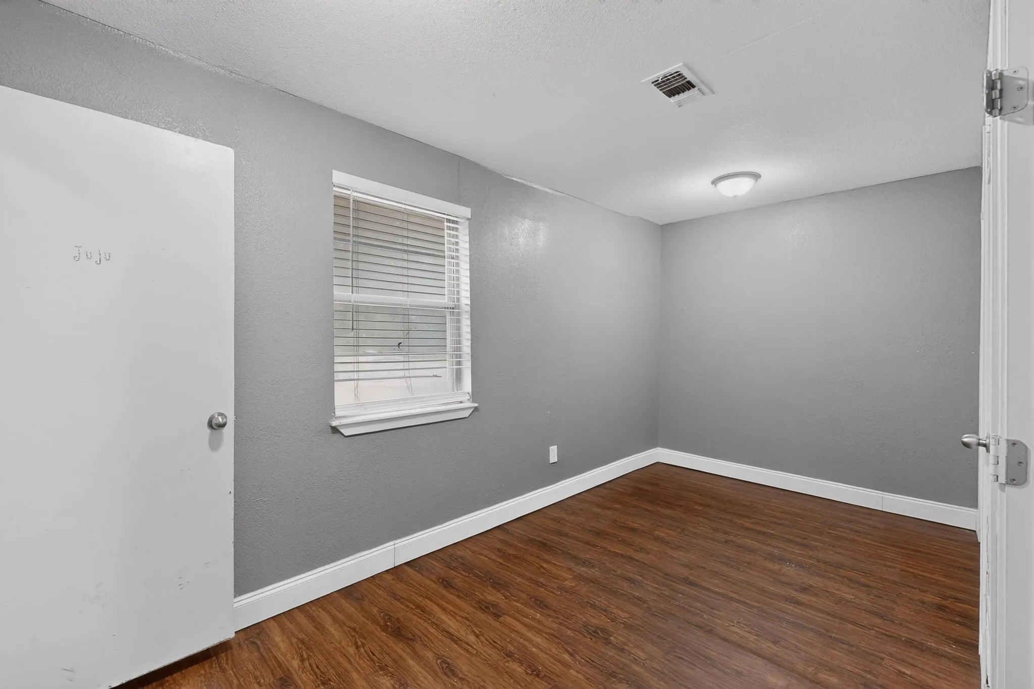Wood-finish flooring, neutral gray walls, window with blinds, ceiling-mounted light fixture