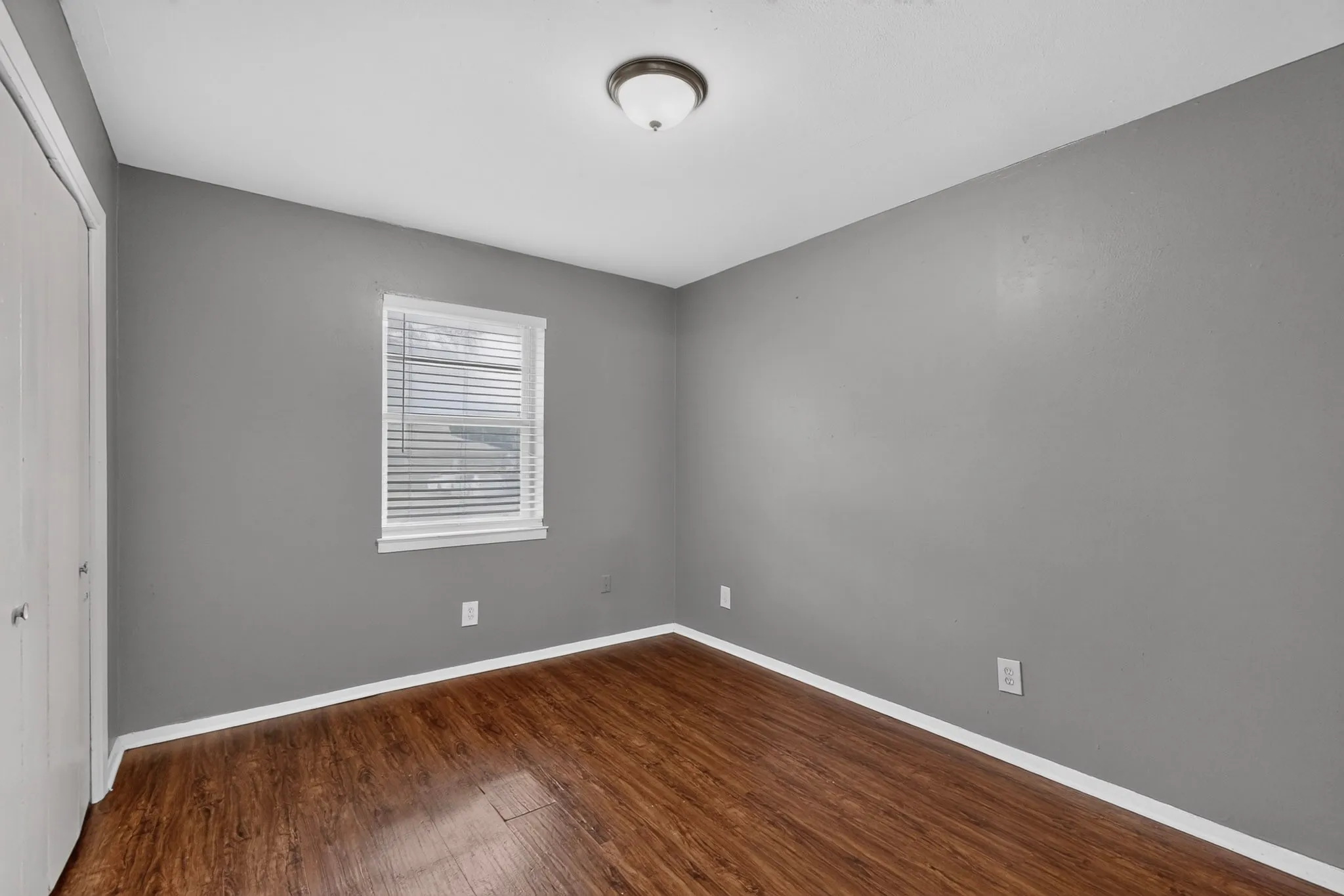 Wood-finish flooring with white trim, gray painted walls, and a white window with blinds