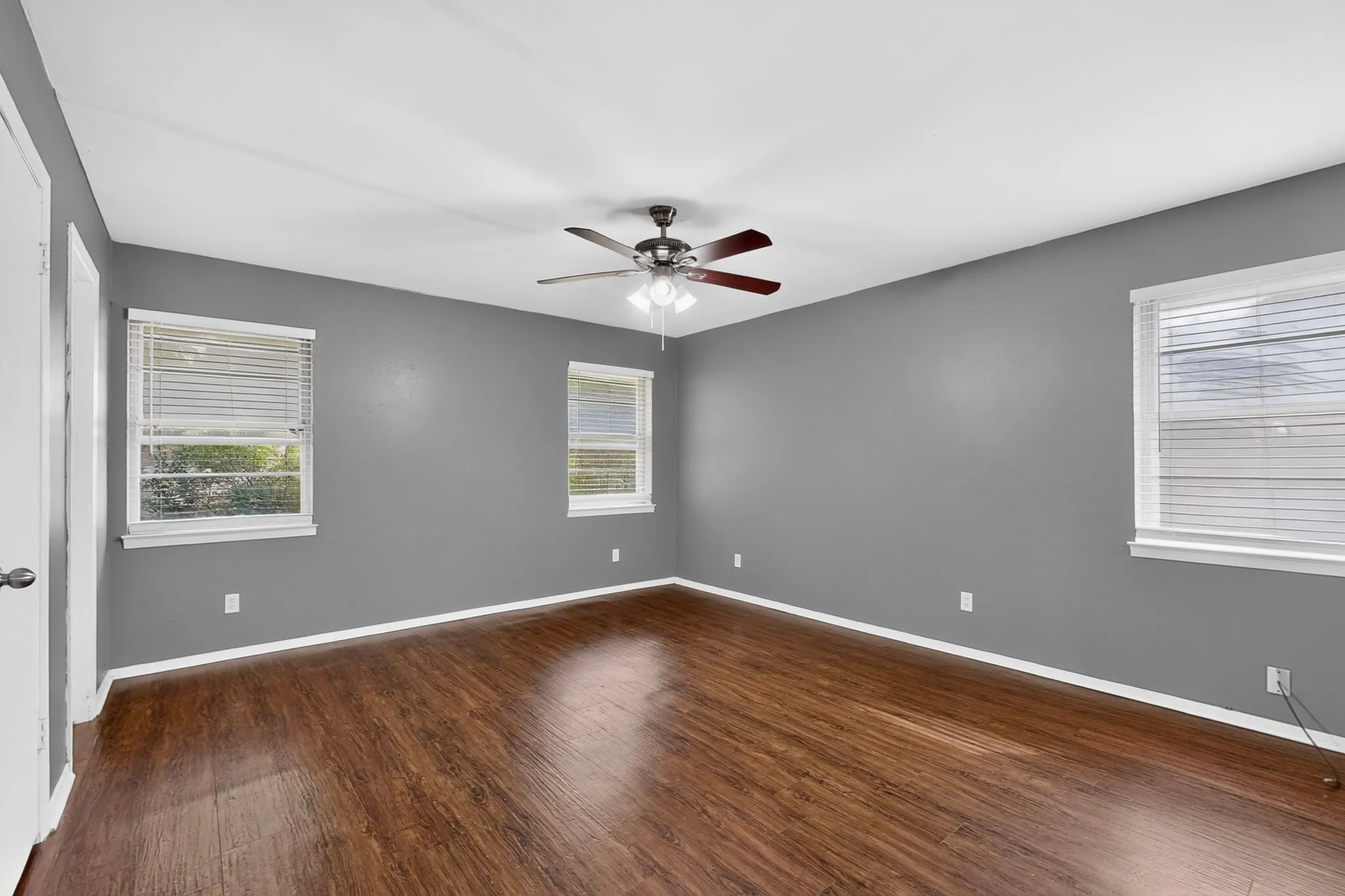 Wood-finish flooring, multiple windows with blinds, ceiling fan, and painted walls
