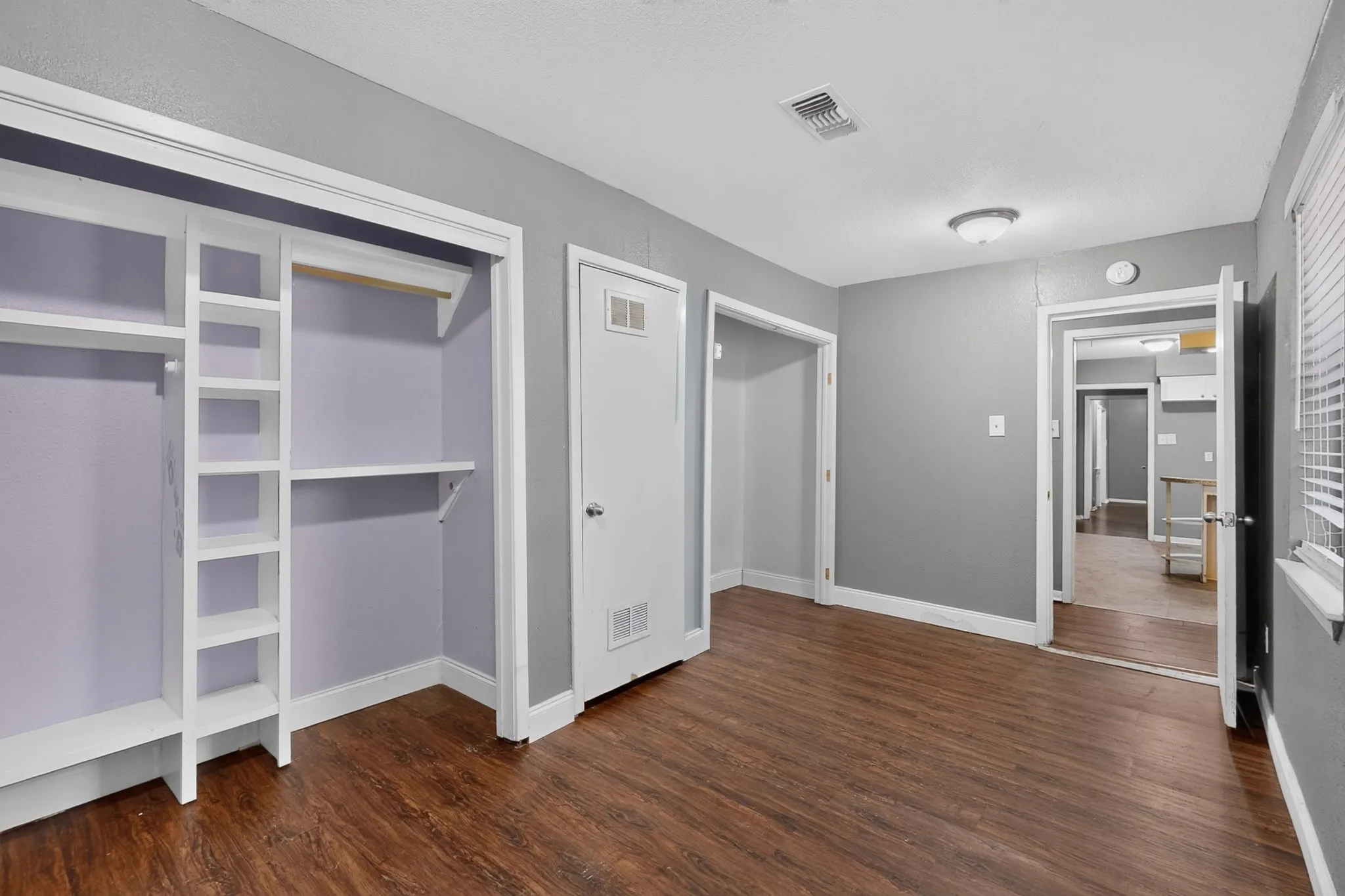 Wood-finish flooring, built-in open shelving, interior white doors, and a ceiling-mounted light fixture