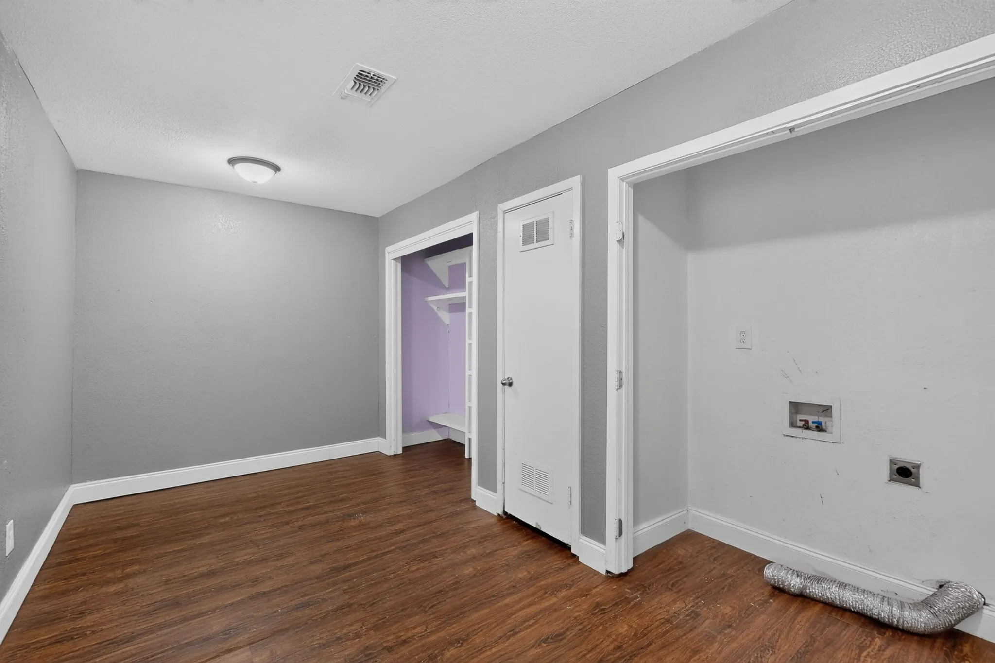 Wood-finish flooring, light grey wall paint, flush mount ceiling fixture, and a built-in closet with shelving