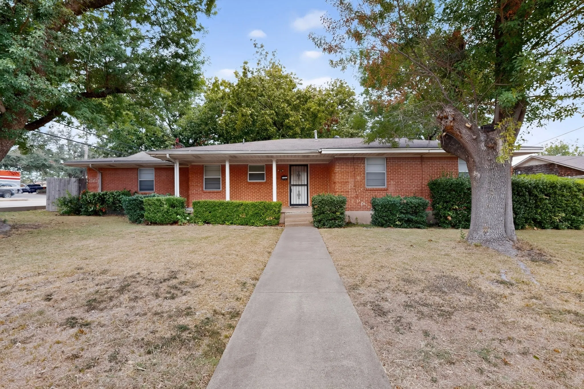 Brick exterior with a covered porch, mature trees, and a concrete pathway