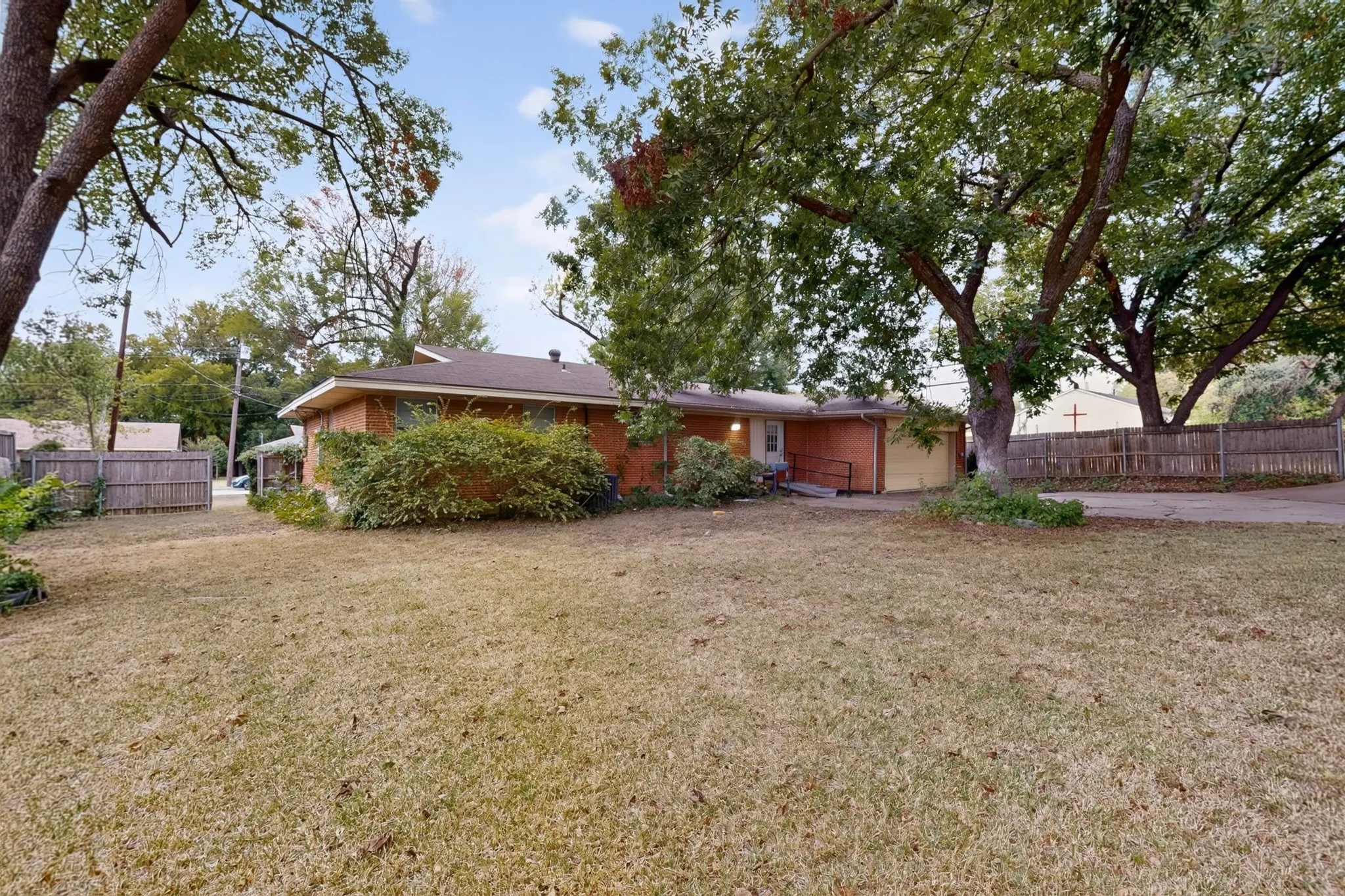 Expansive front lawn with mature trees and a brick exterior residence