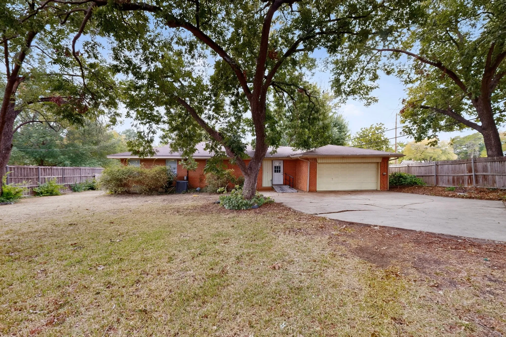 Brick exterior residence with a concrete driveway, attached garage, and mature trees
