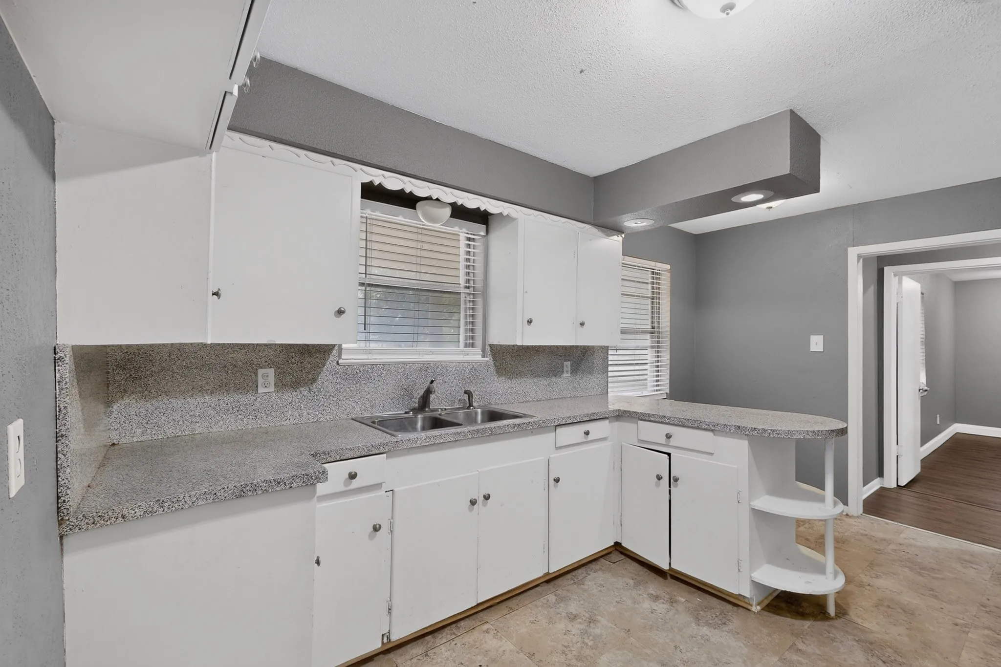 Bright kitchen featuring white cabinetry, speckled stone countertops, stainless steel sink with single-handle faucet, and tile backsplash