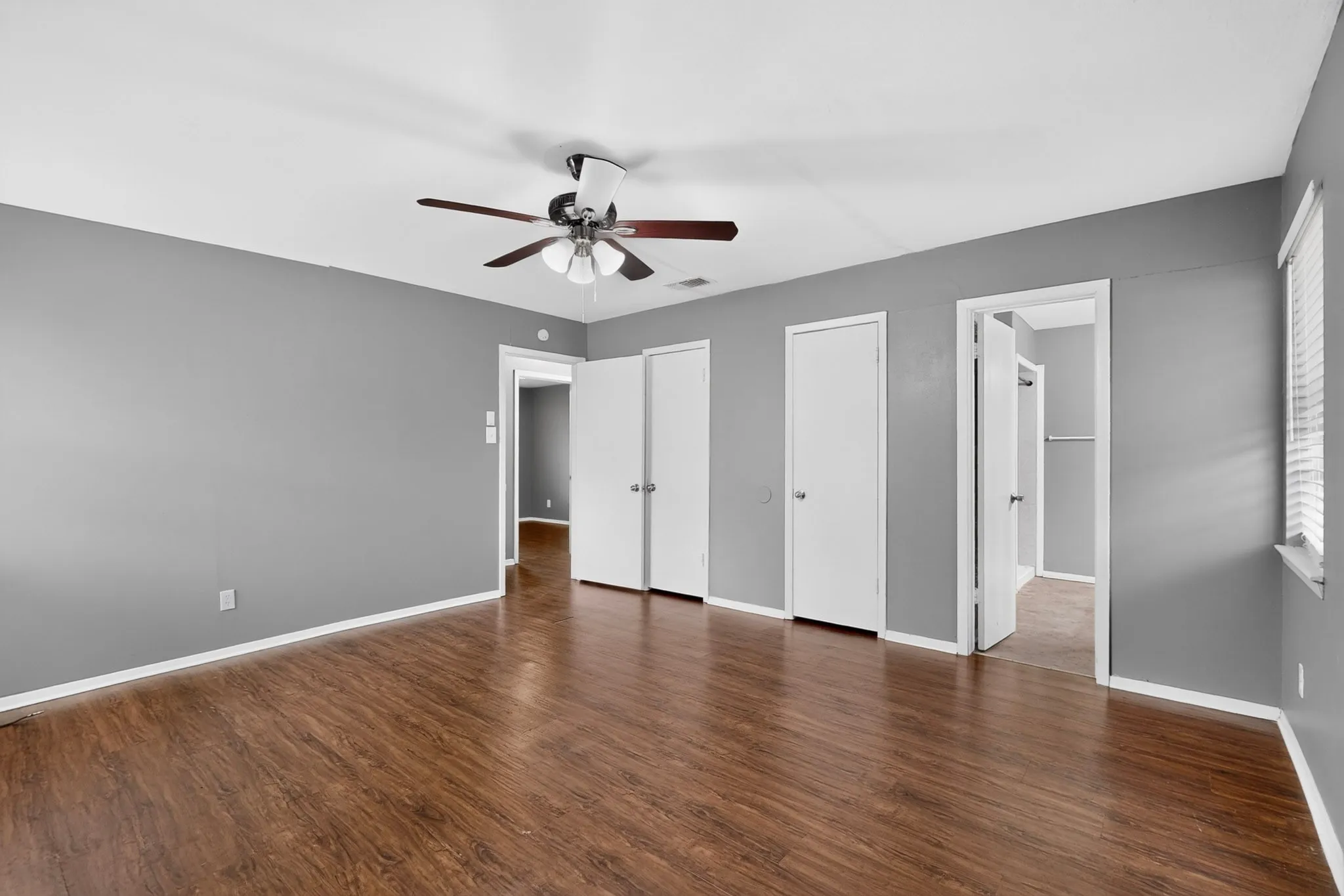 Wood-finish flooring, ceiling fan with light fixture, and multiple white doors