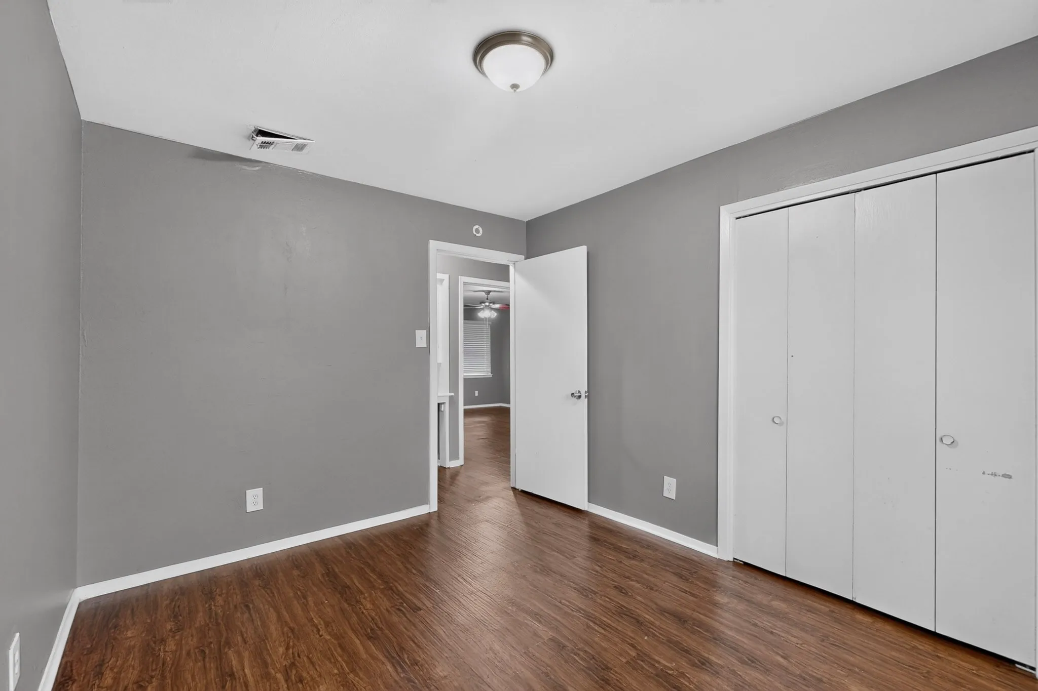 Wood-finish flooring with white trim, grey wall paint, and overhead lighting