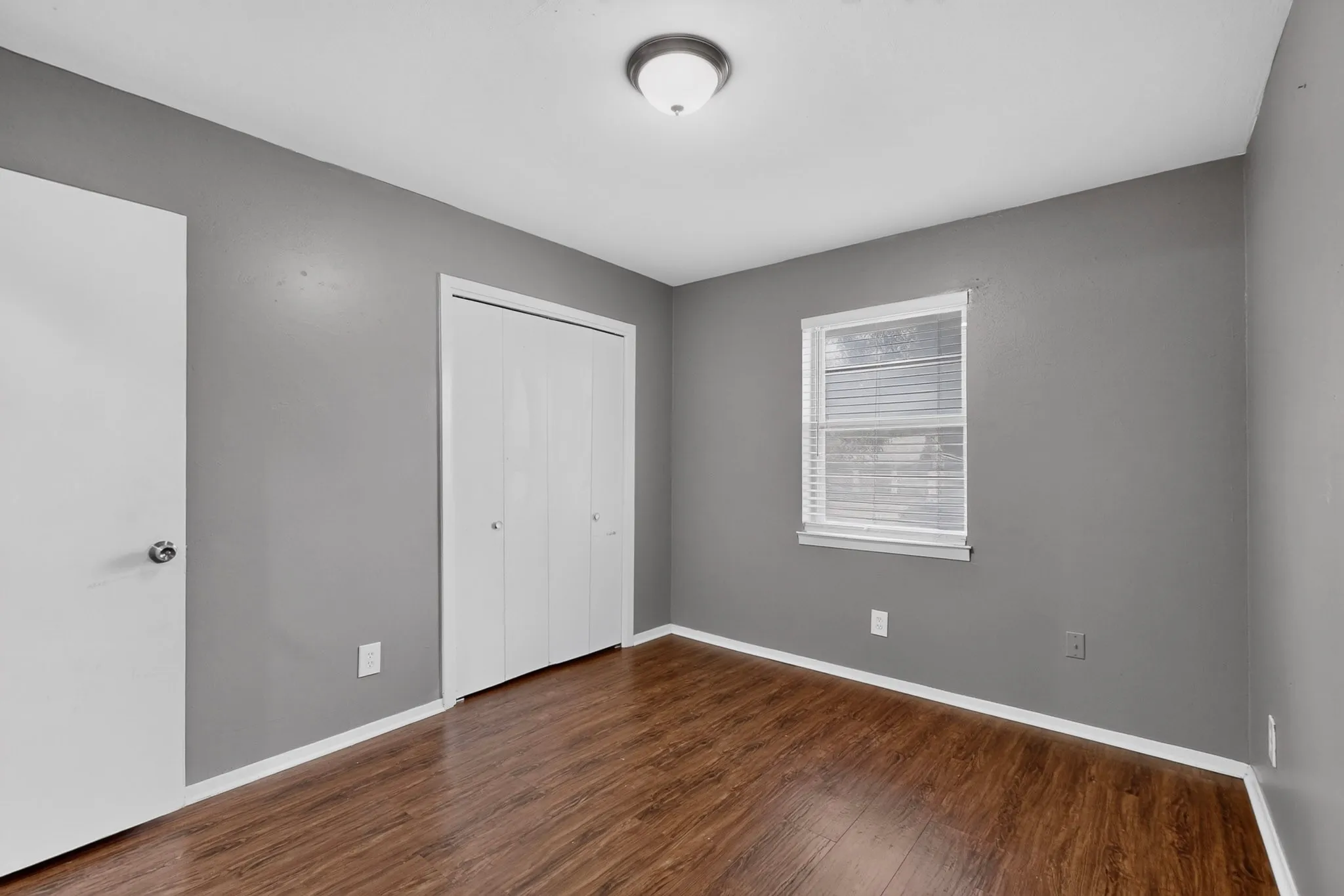 Wood-finish flooring, neutral gray wall tones, white trim, and a window with blinds