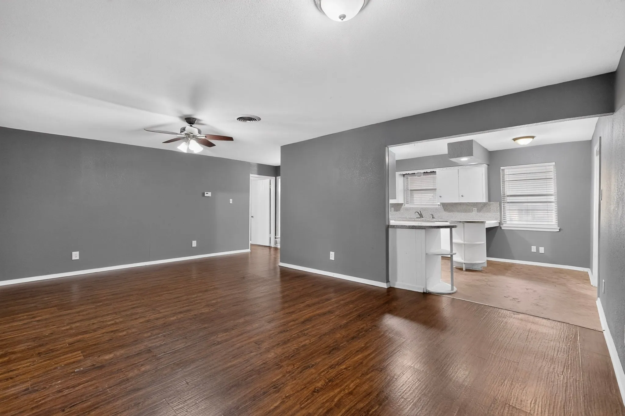 Open-concept living space featuring warm wood-finish flooring throughout, ceiling fan with integrated lighting, and gray-painted walls