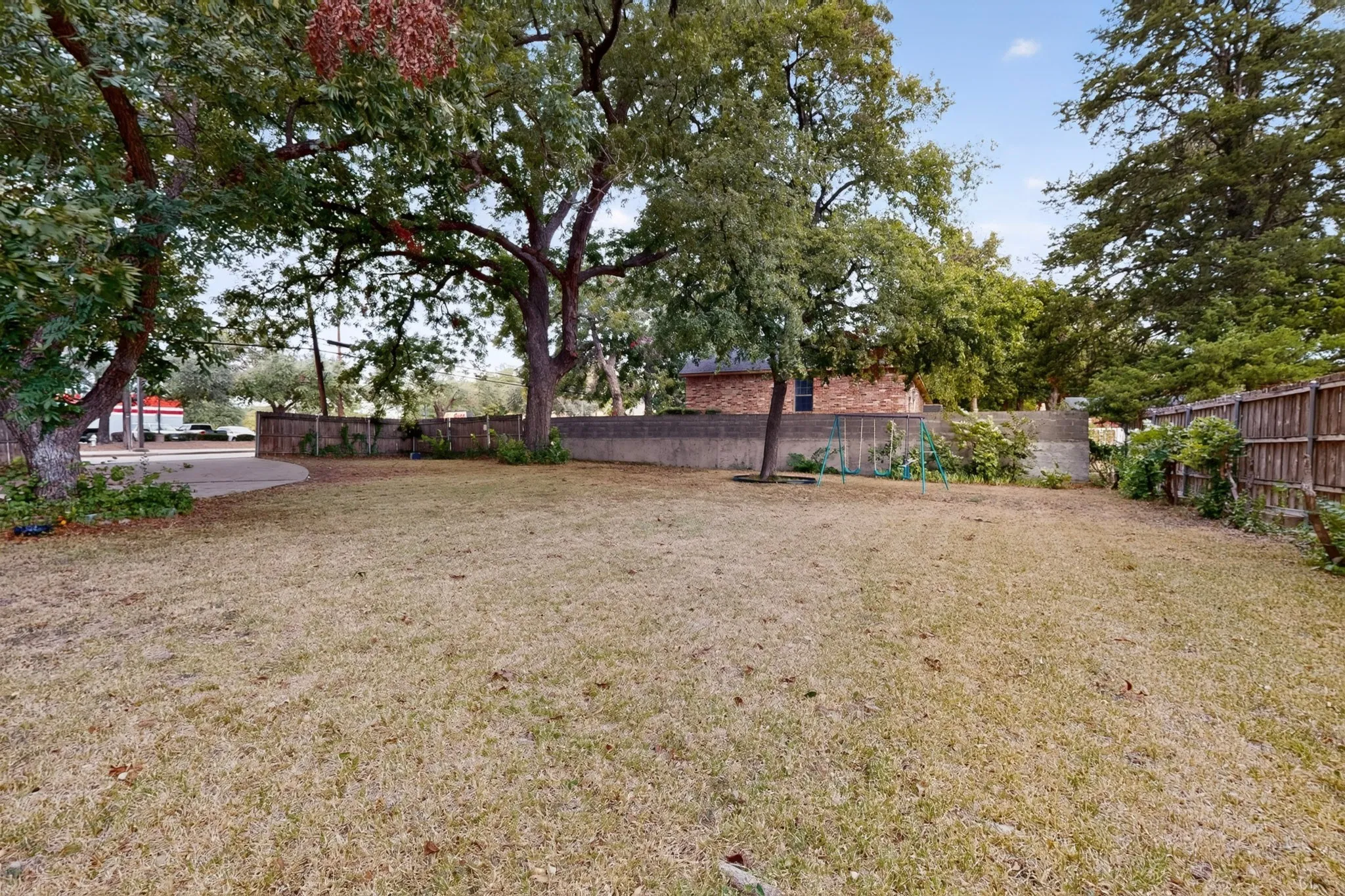 Expansive outdoor space featuring a large lawn area, mature trees, and a wooden privacy fence